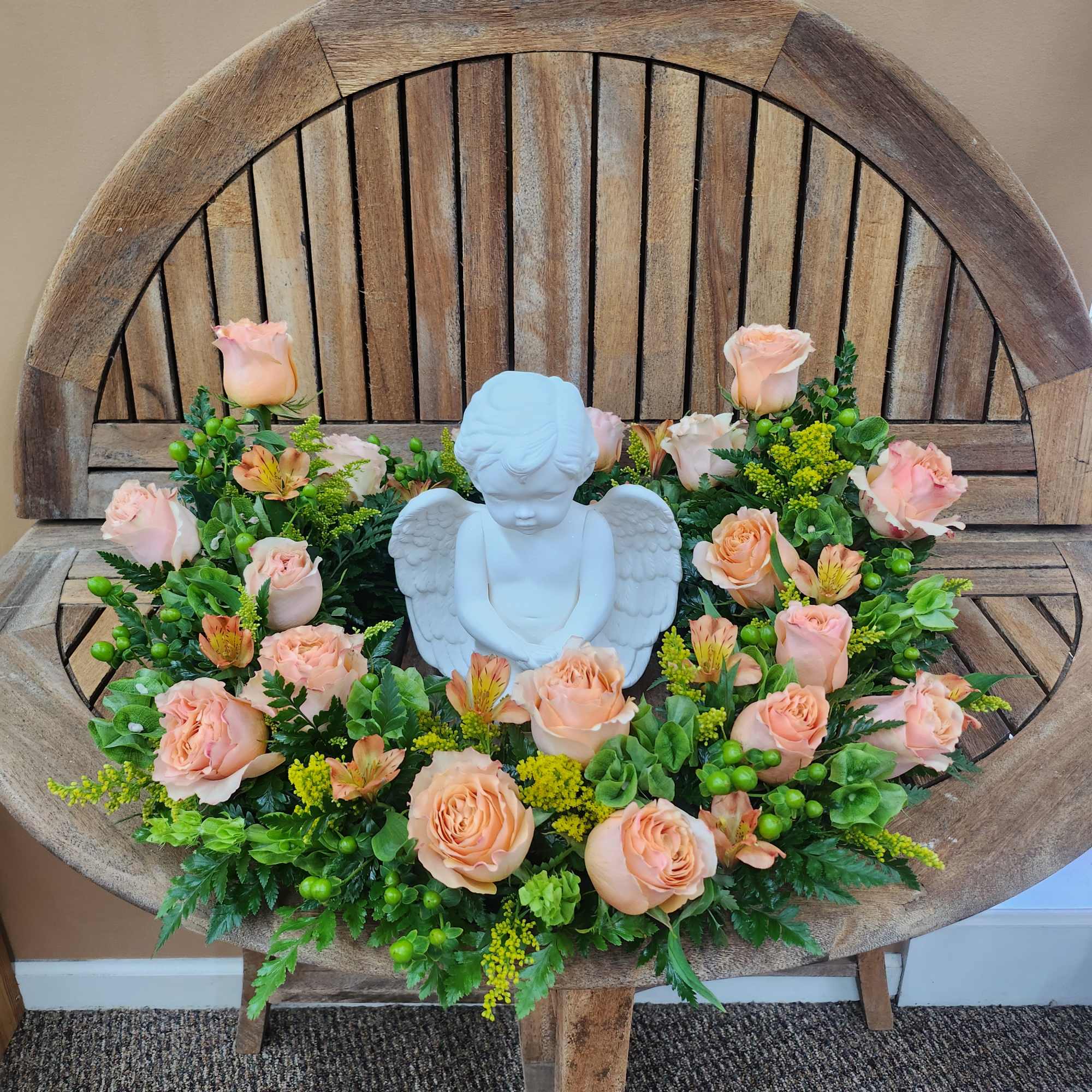 Peach roses arranged around a white angel figurine on a wooden chair