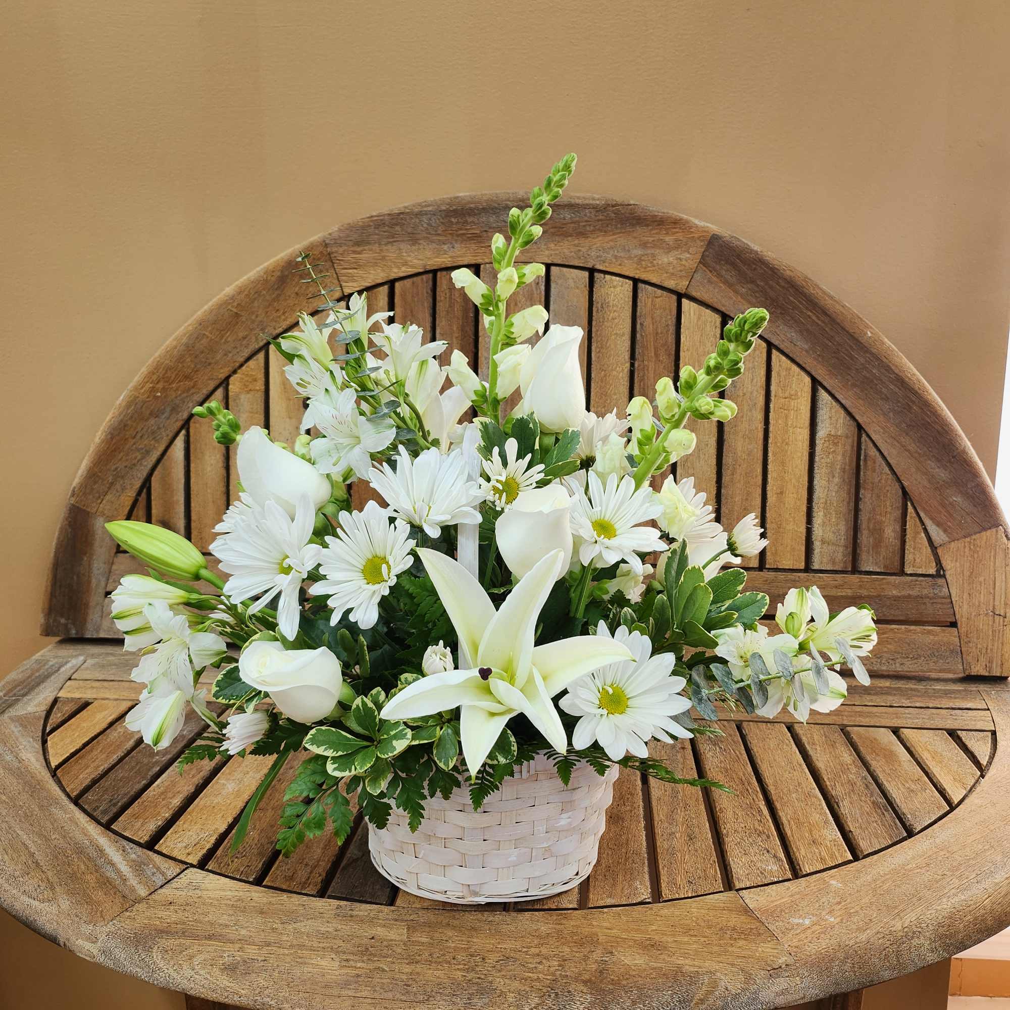 White floral arrangement in a woven basket on a wooden bench