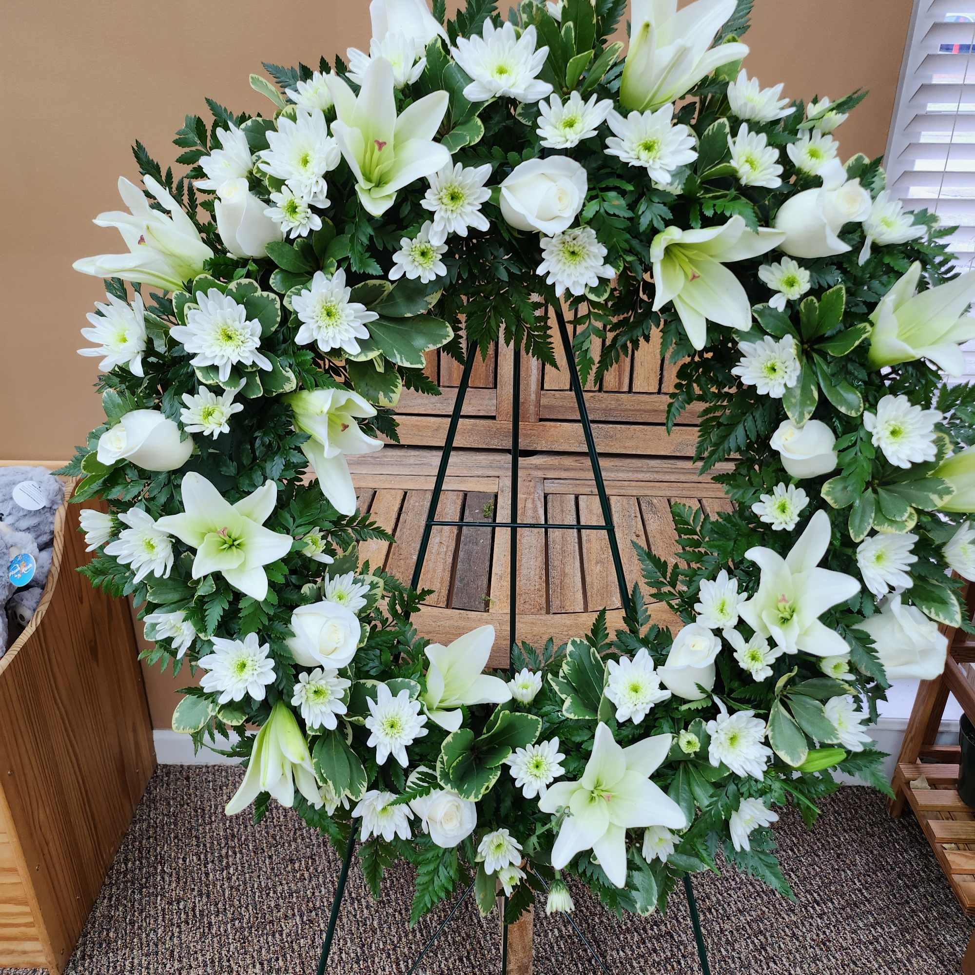 White floral wreath on a stand with lilies and daisies