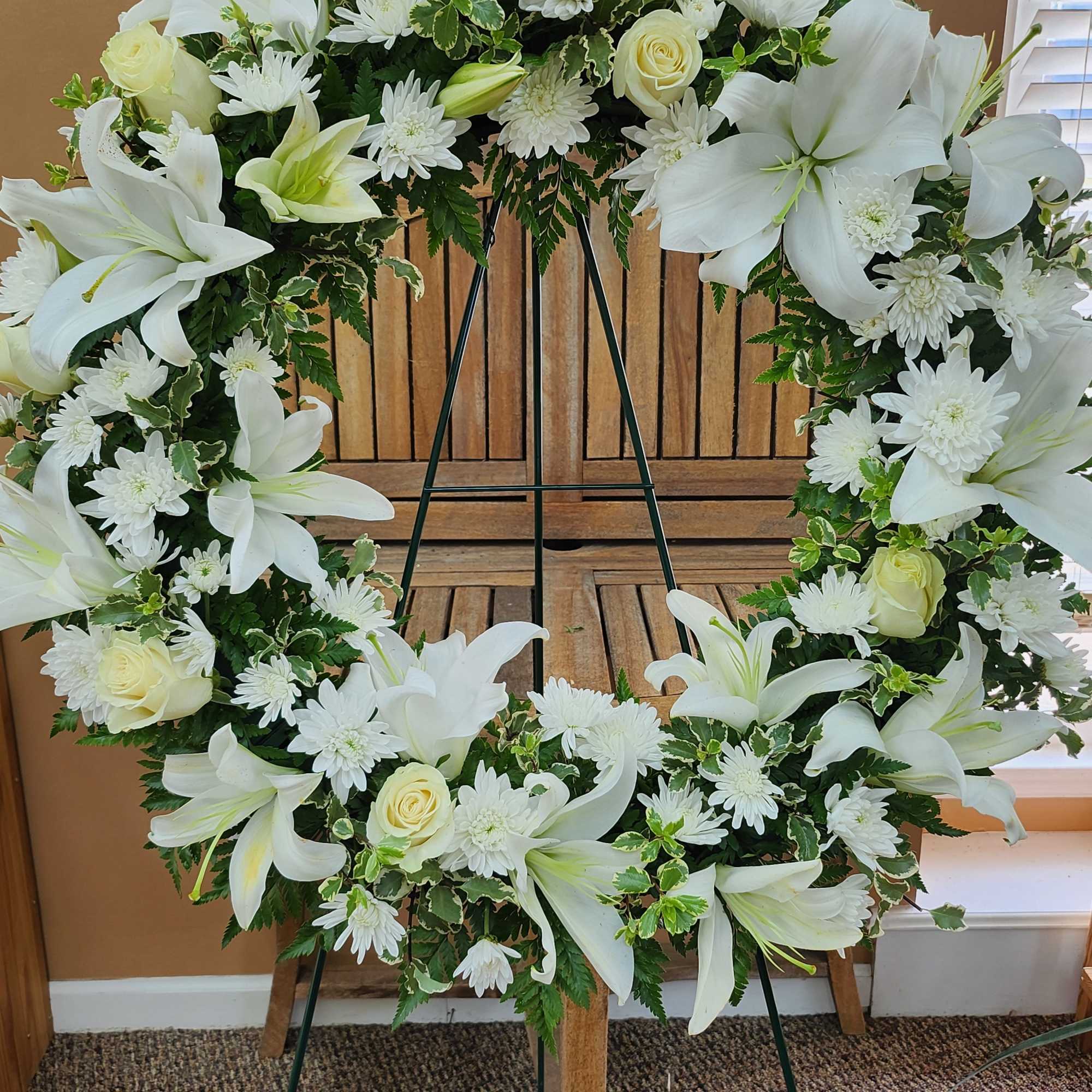White floral wreath on a stand with lilies, roses, and daisies