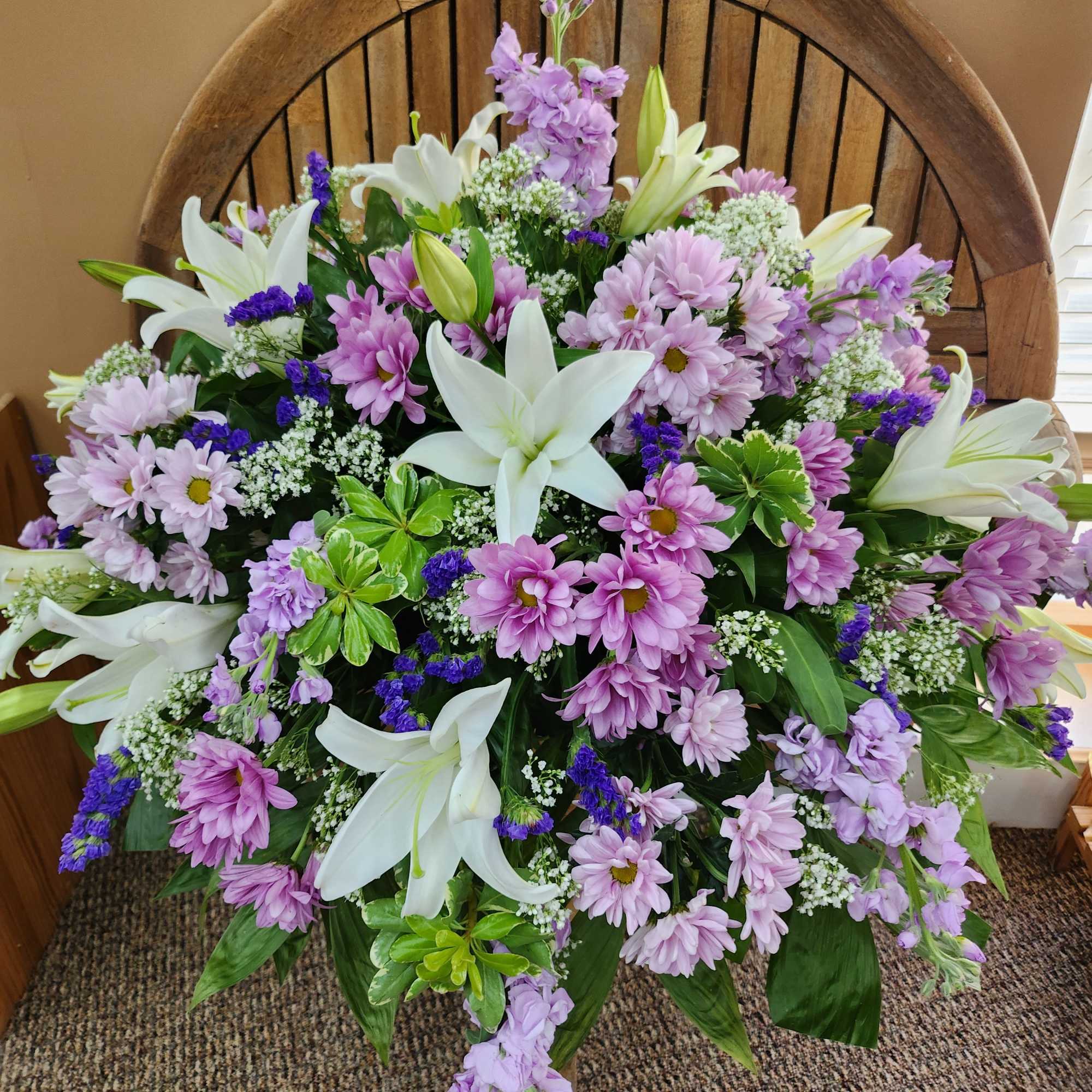 Lavender and white floral arrangement with lilies and daisies in front of a wooden chair