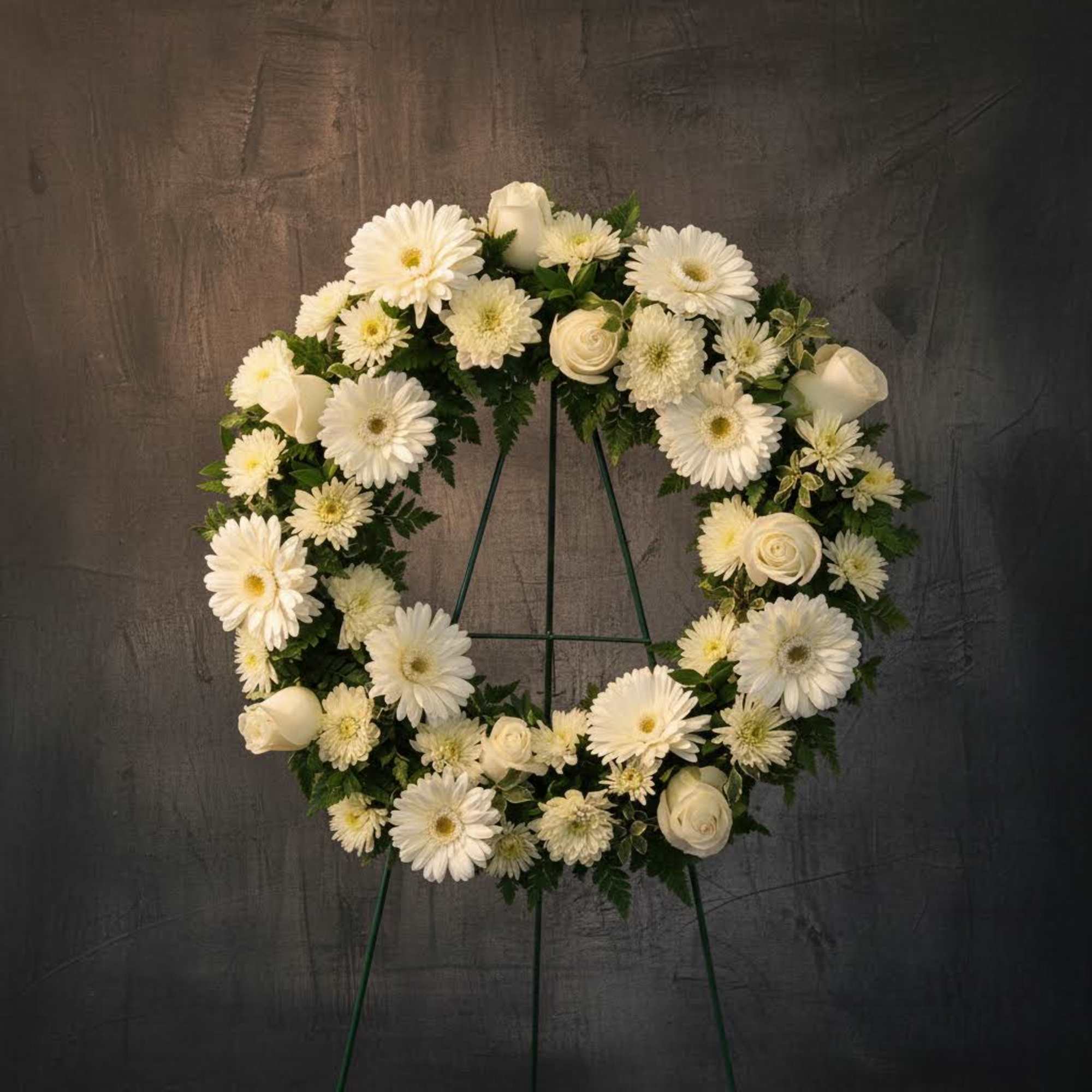 White floral wreath on a stand with daisies and roses