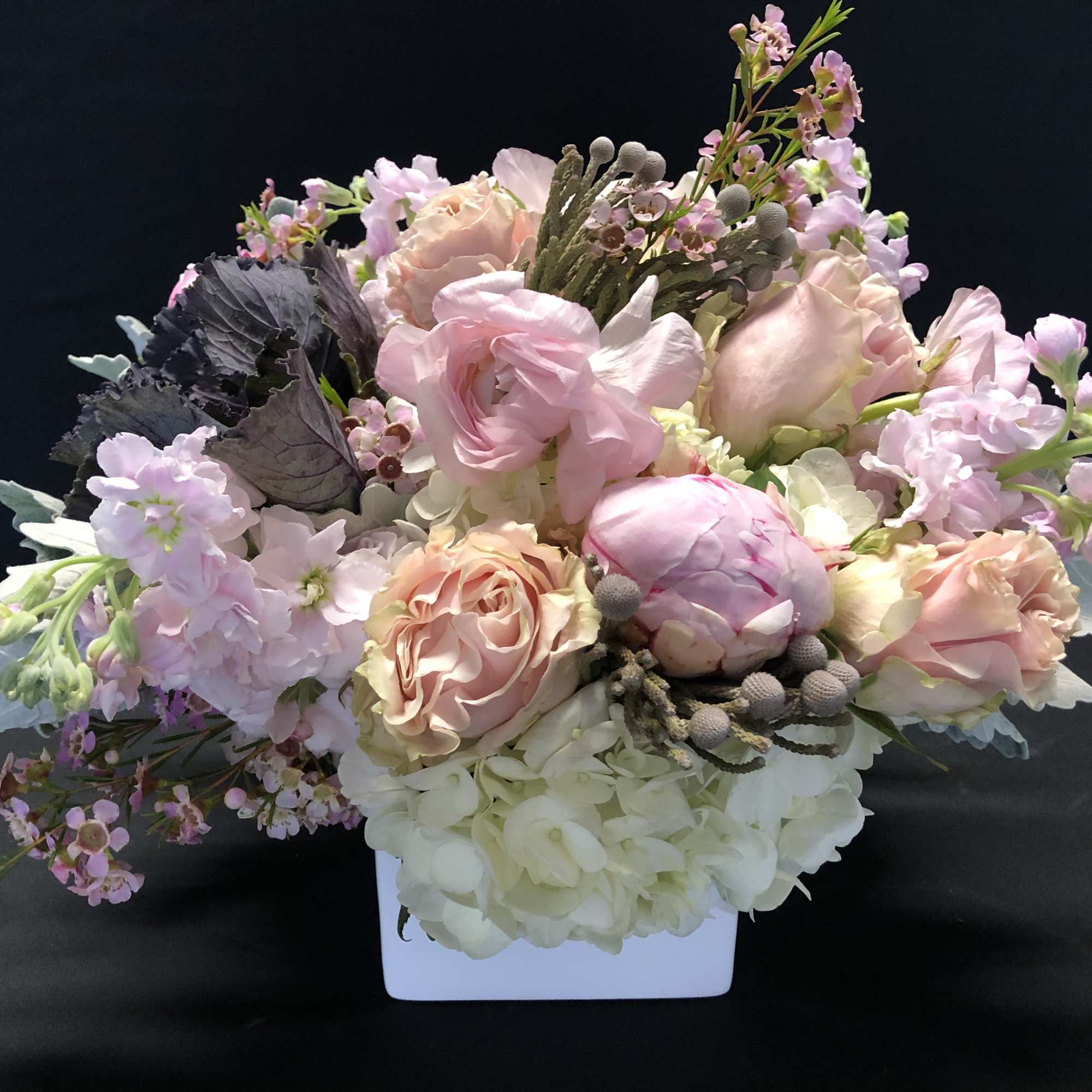 Low arrangement of blush pink and white roses, peonies, stock, and hydrangea in a white rectangular vase