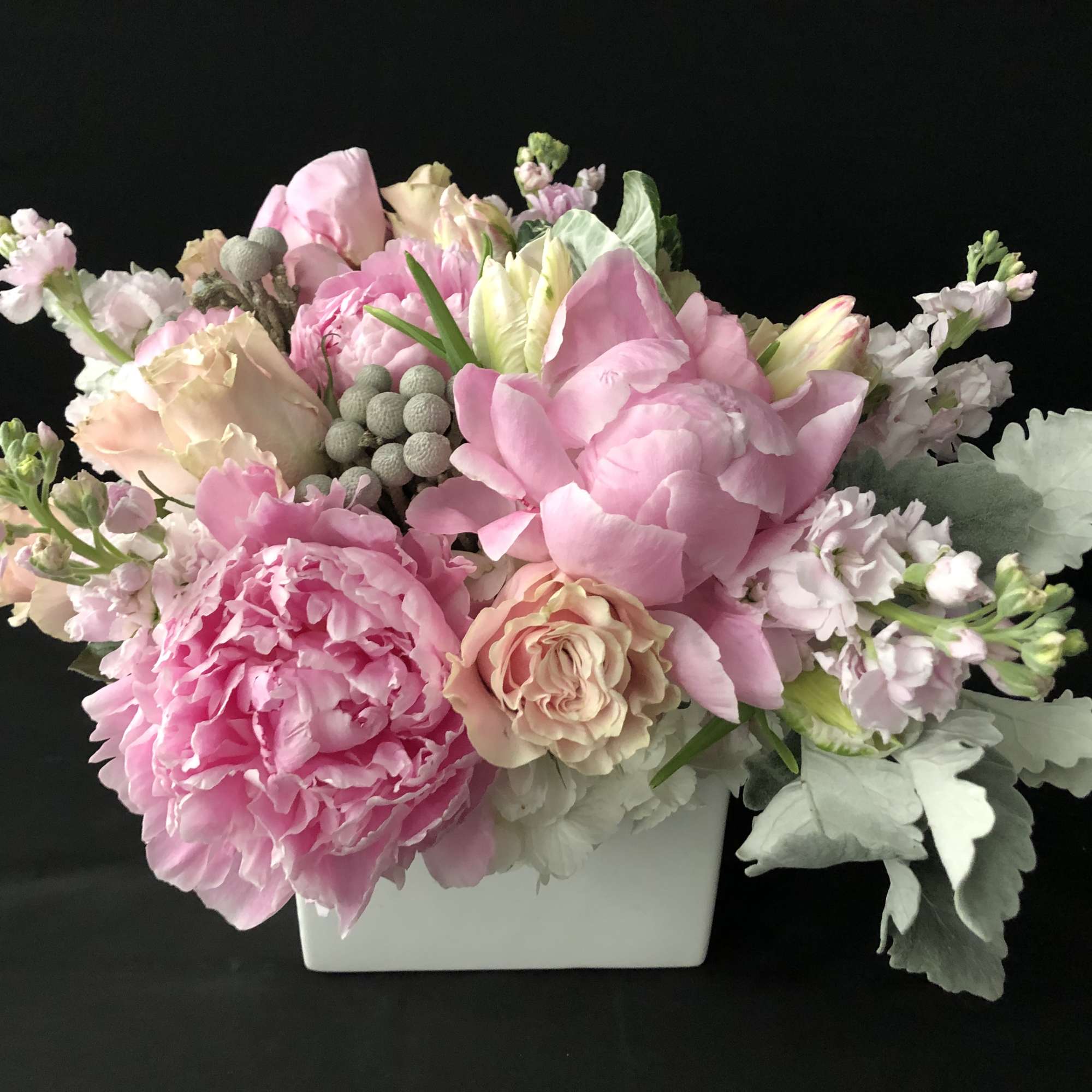 Low square arrangement of pink peonies, blush roses, and pastel blooms in a white ceramic vase