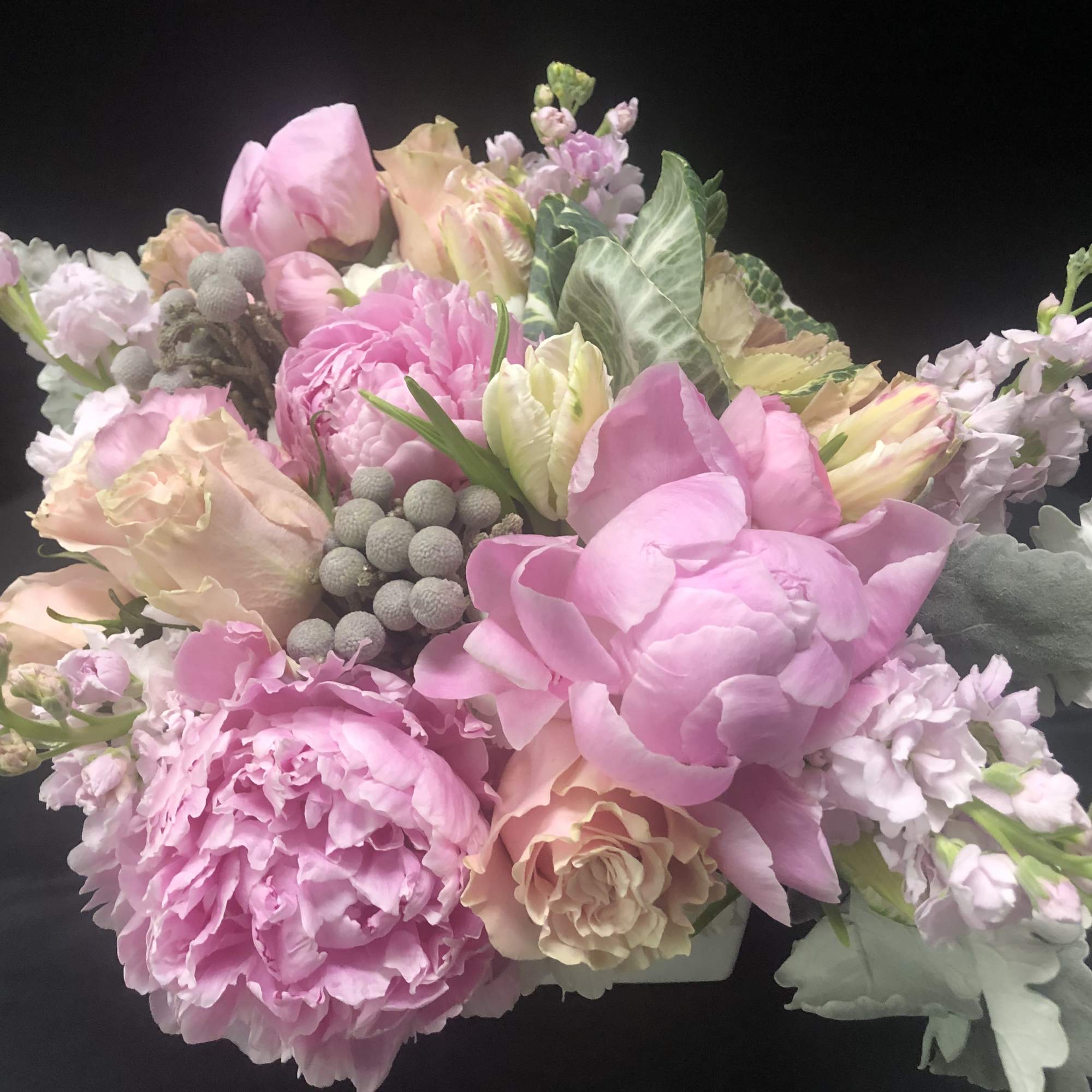Low pink and peach bouquet with peonies, roses, and accent blooms in a compact arrangement.