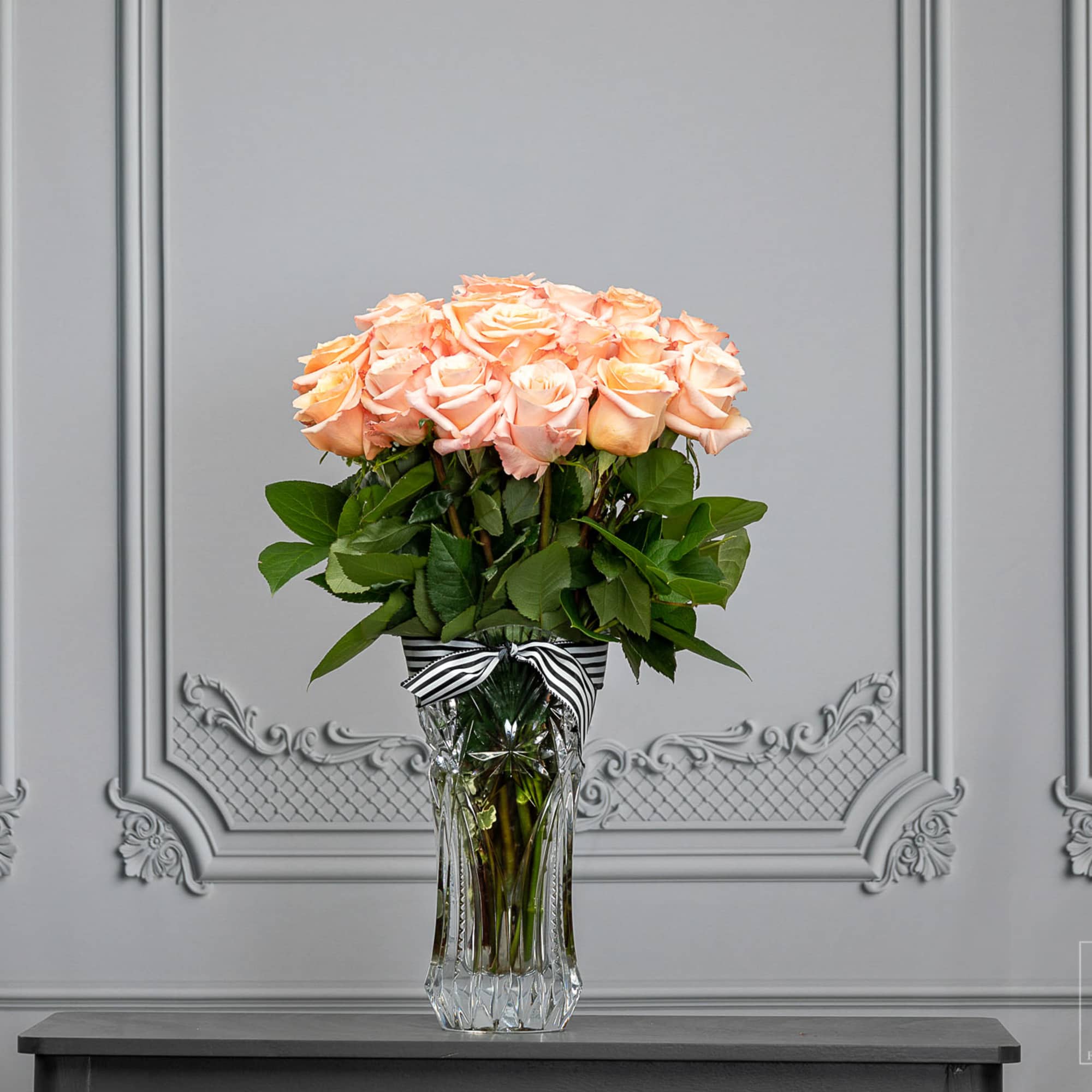 Peach roses arranged in a clear glass vase with a striped ribbon