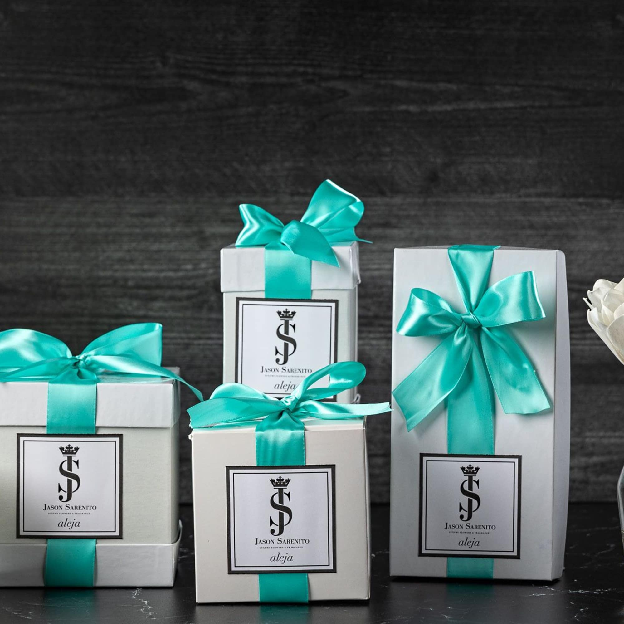 Gift boxes with teal ribbons beside a candle and a small vase of white flowers