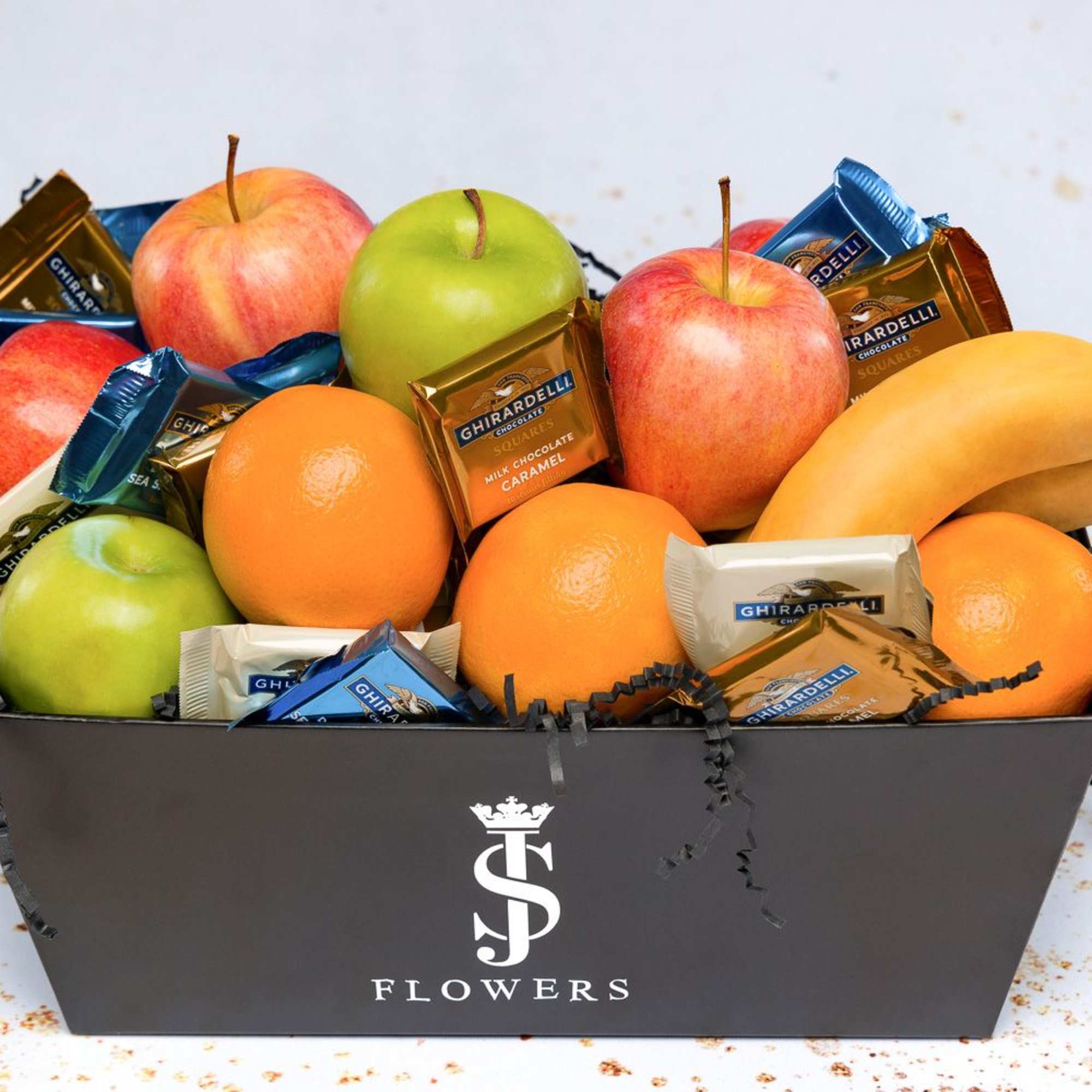 Gift box with apples, bananas, oranges, and wrapped chocolates