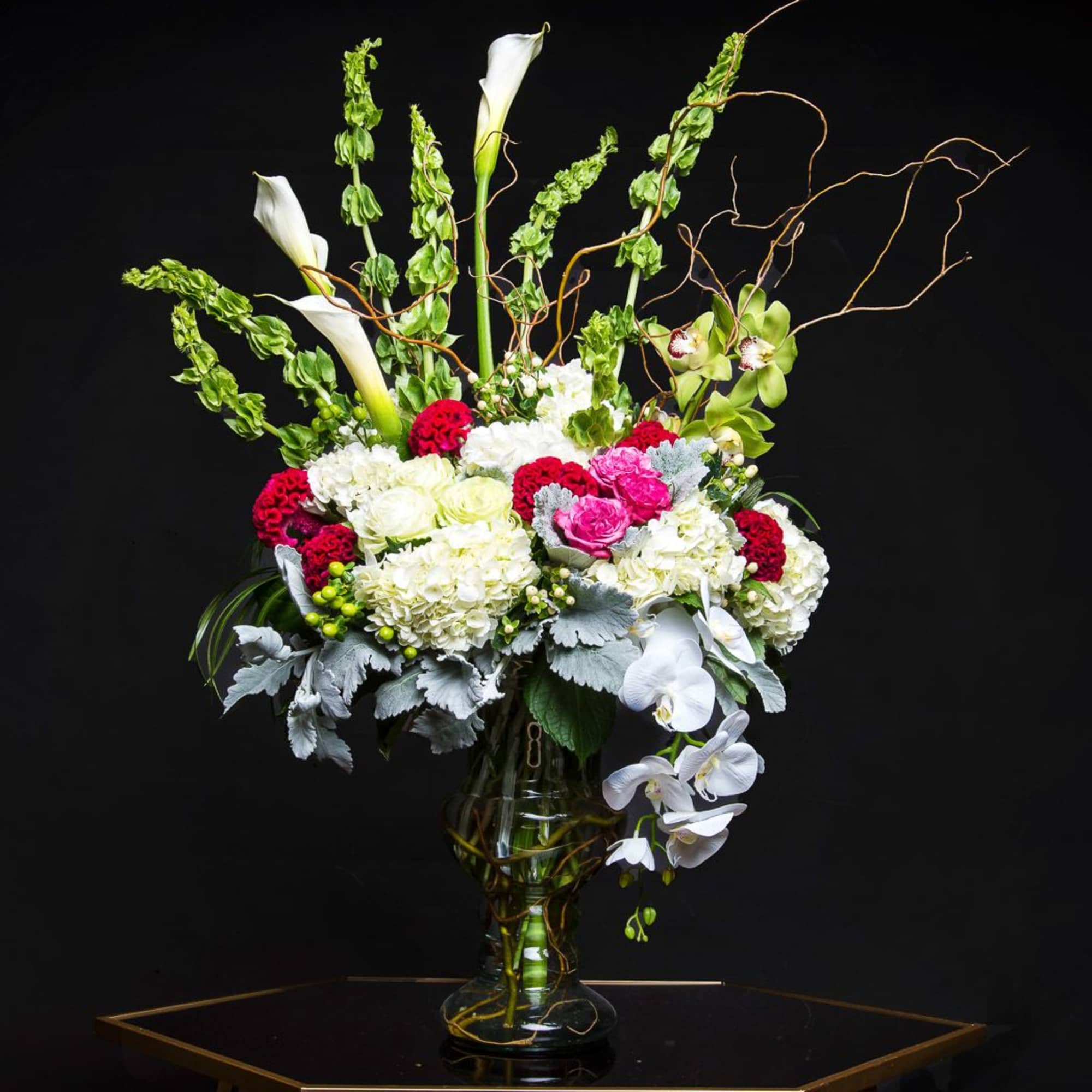Tall floral arrangement in a glass vase with white calla lilies and orchids