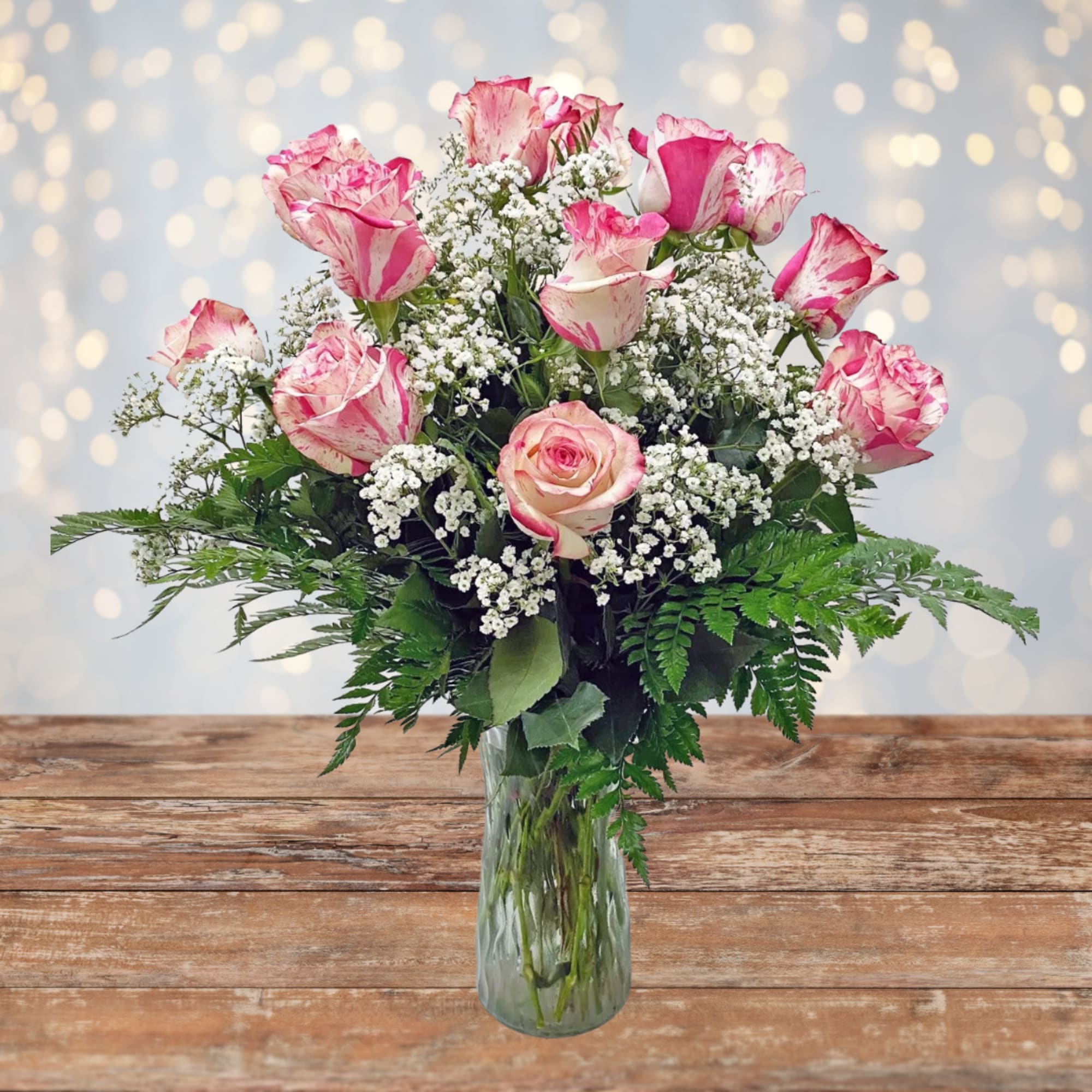 Arrangement of pink and white roses with small white filler flowers in a clear glass vase.