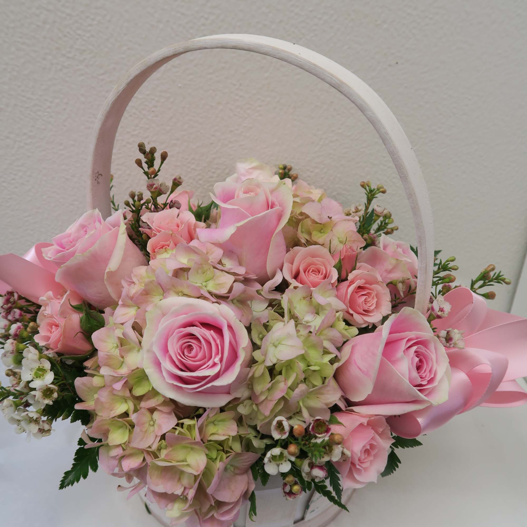 Pink roses and hydrangeas arranged in a white basket with a ribbon handle
