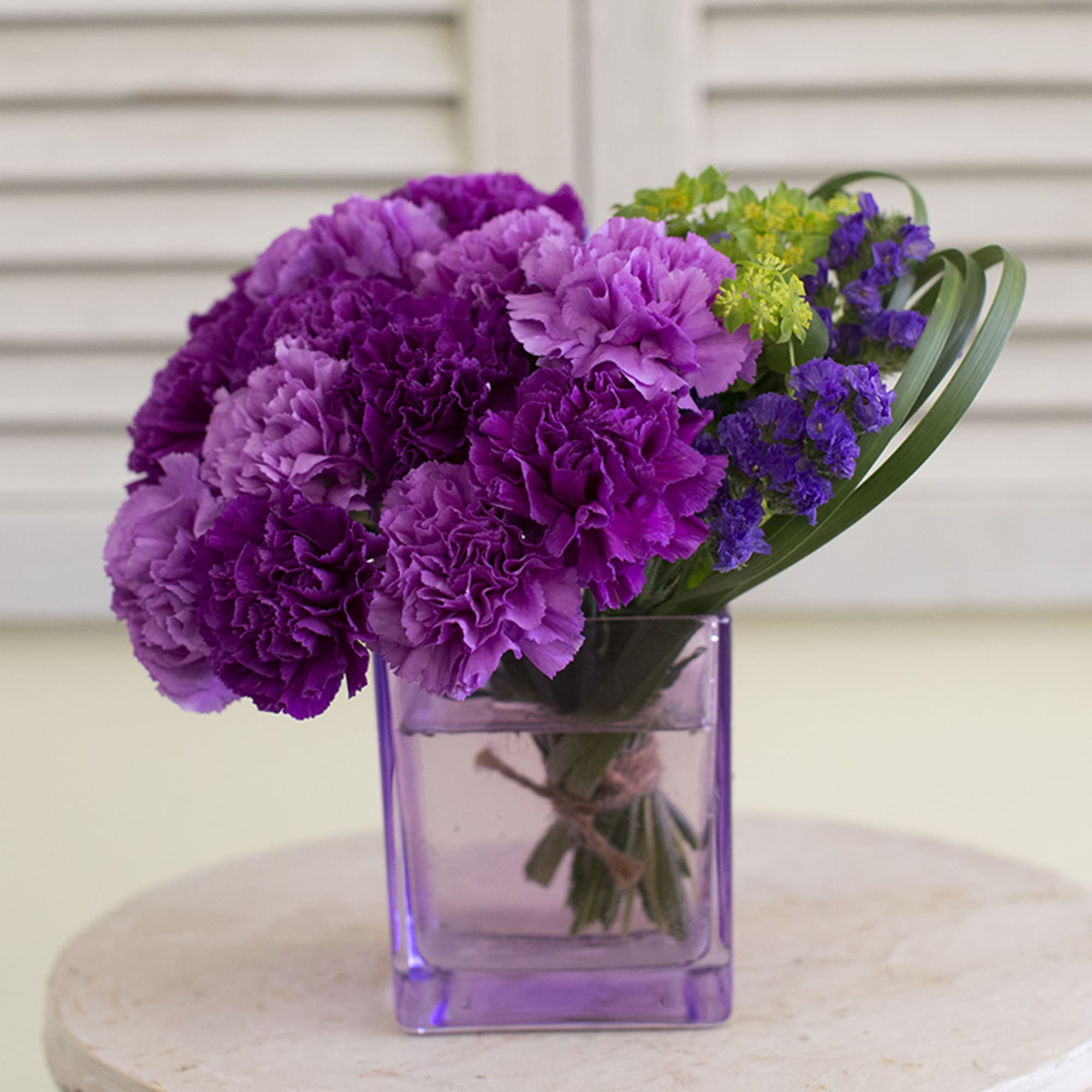Purple carnations in a square glass vase with small purple and green filler flowers