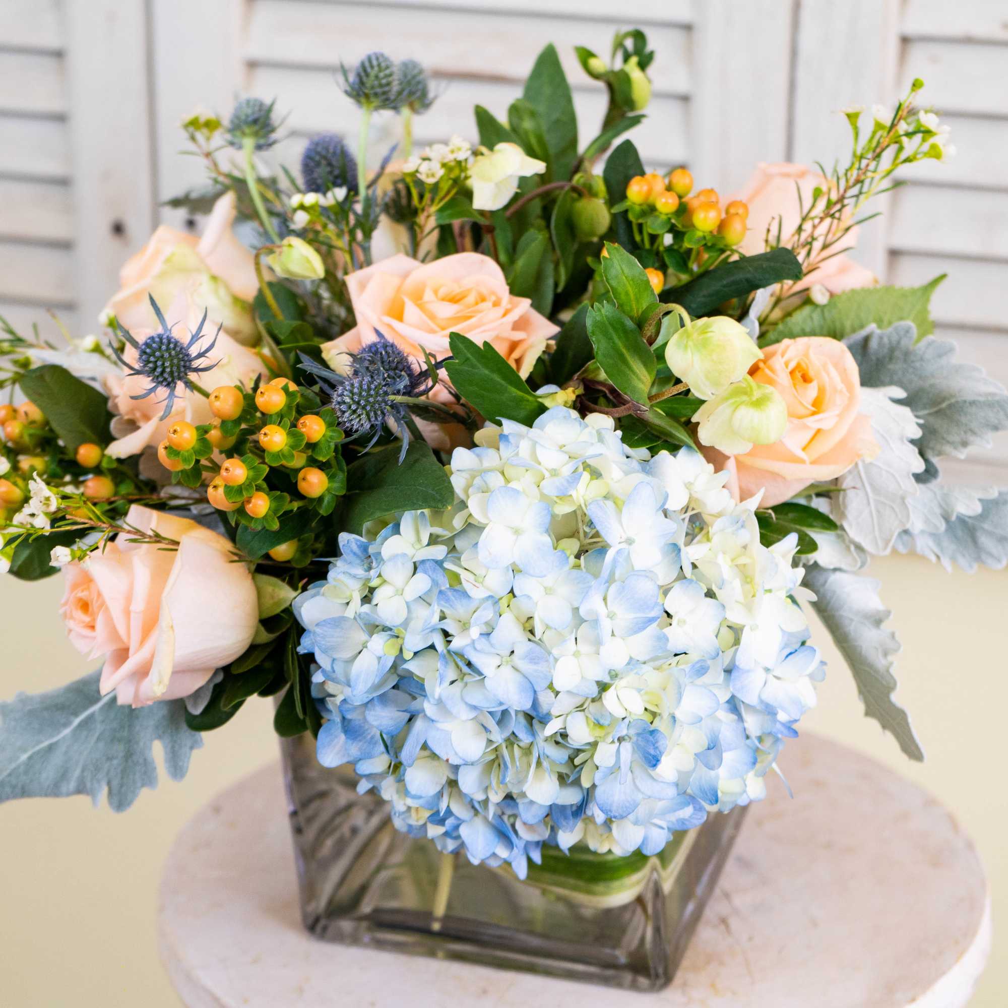 Pastel roses and blue hydrangeas in a square glass vase