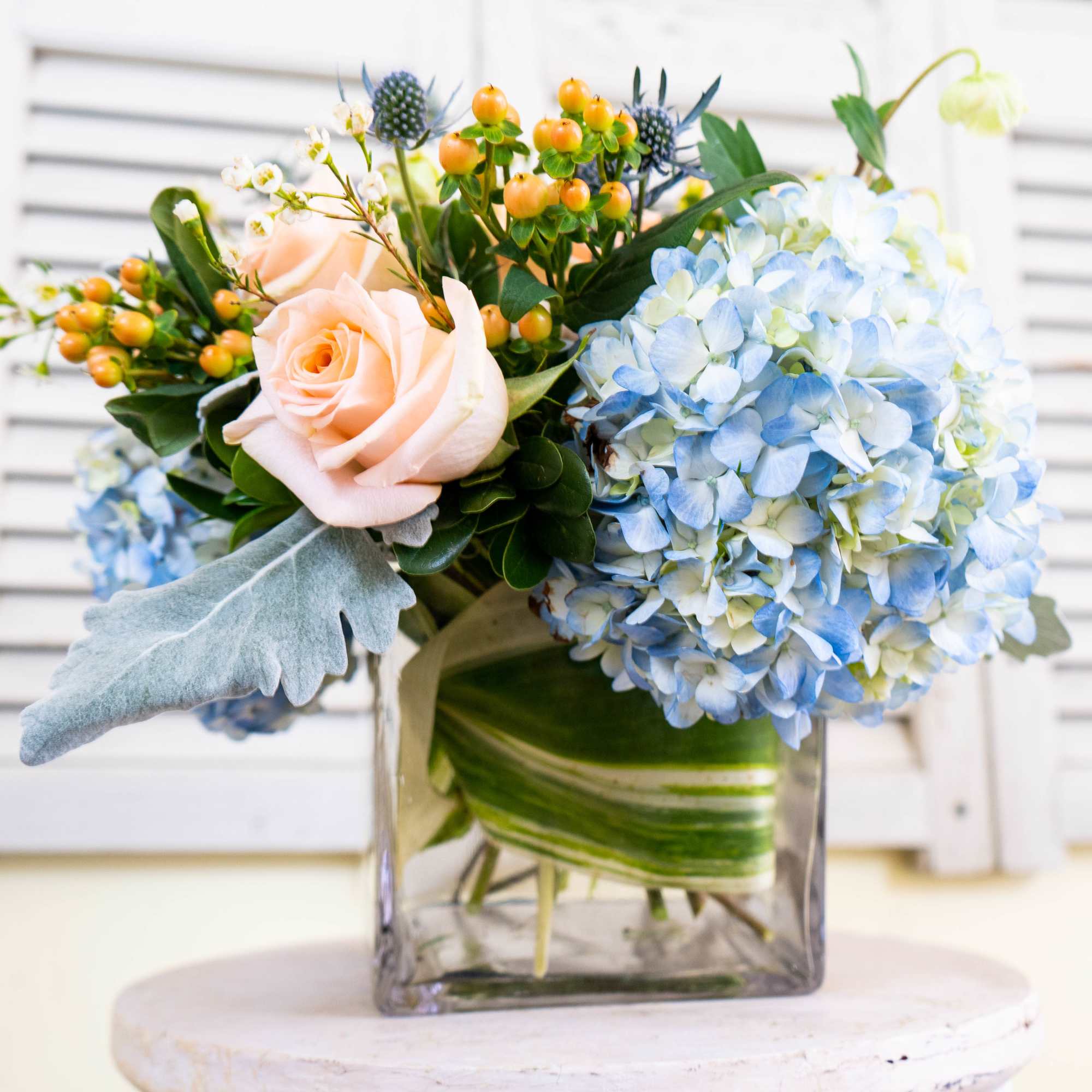 Blue hydrangeas and peach roses in a square glass vase