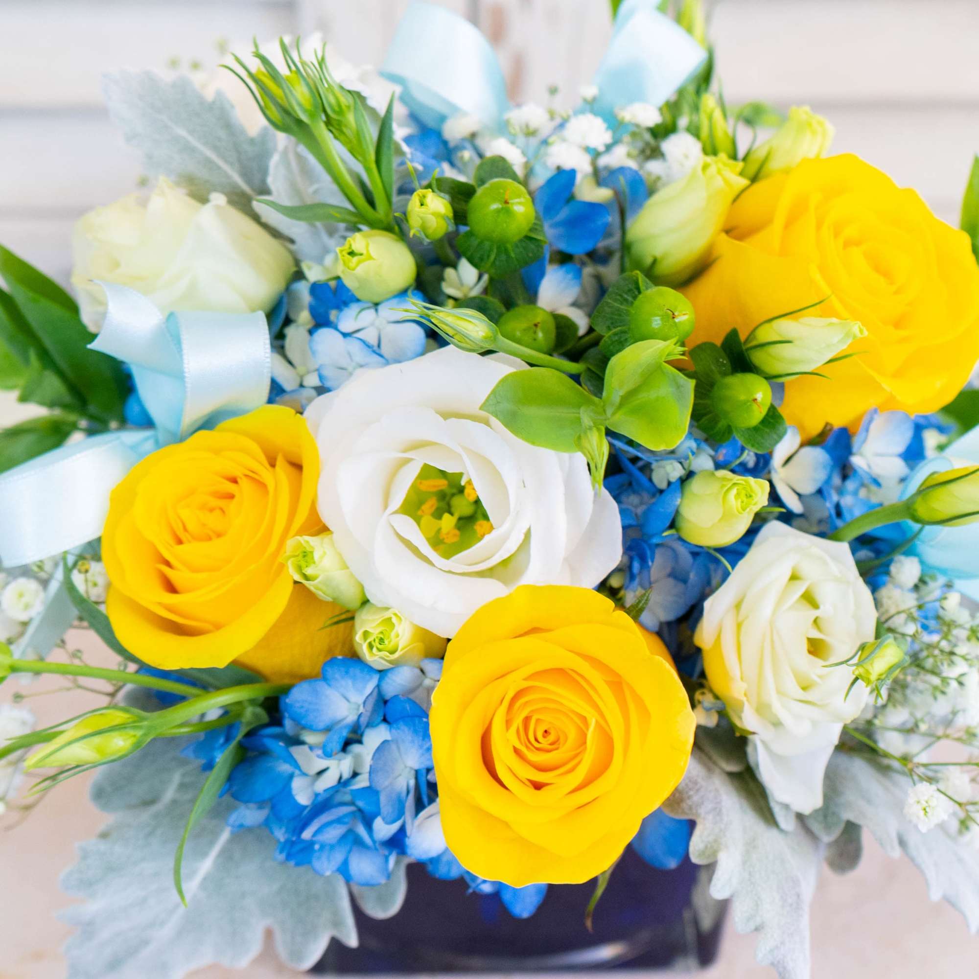 Bouquet of yellow and white roses with blue flowers and ribbon