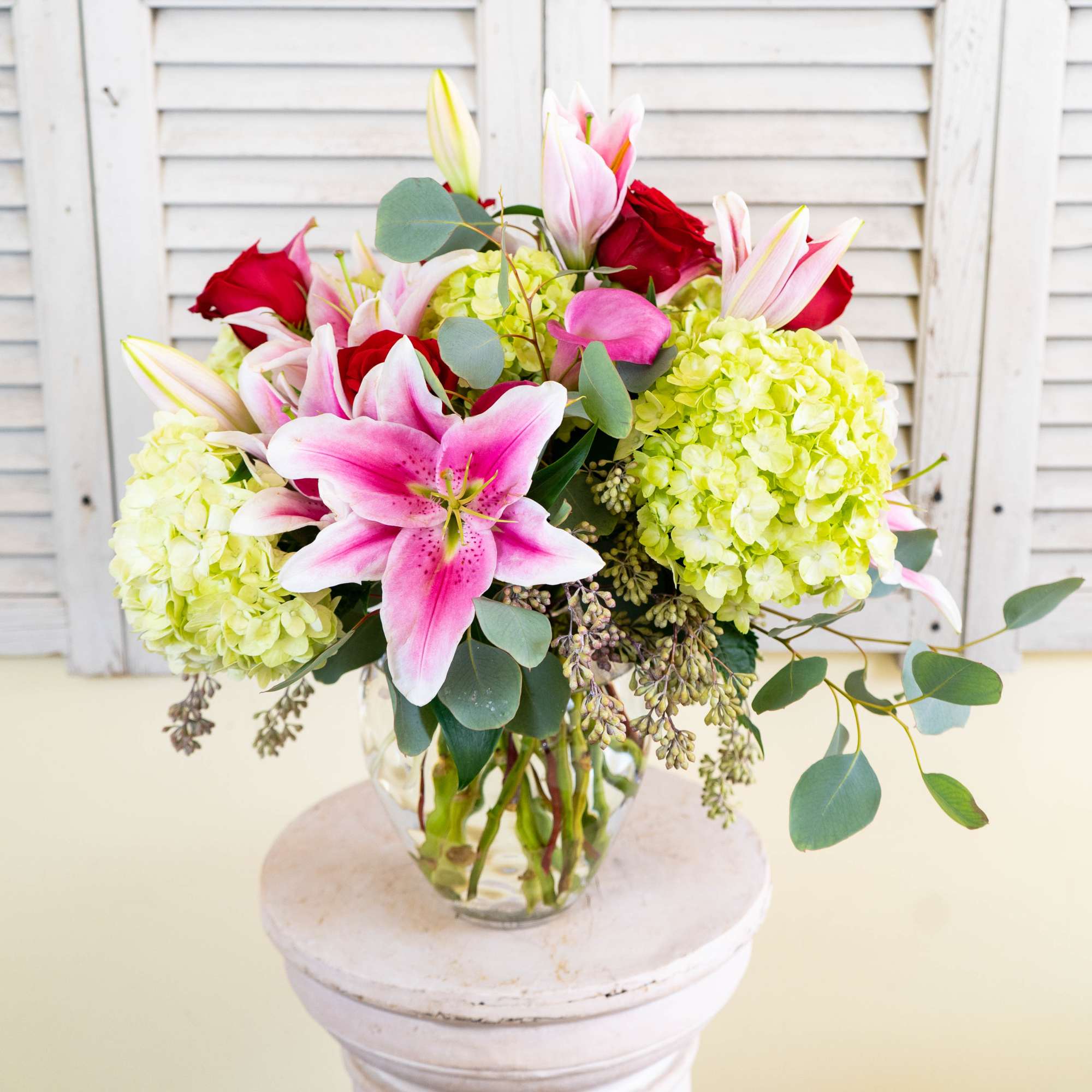 Bouquet of pink lilies, red roses, and pale green hydrangeas in a glass vase