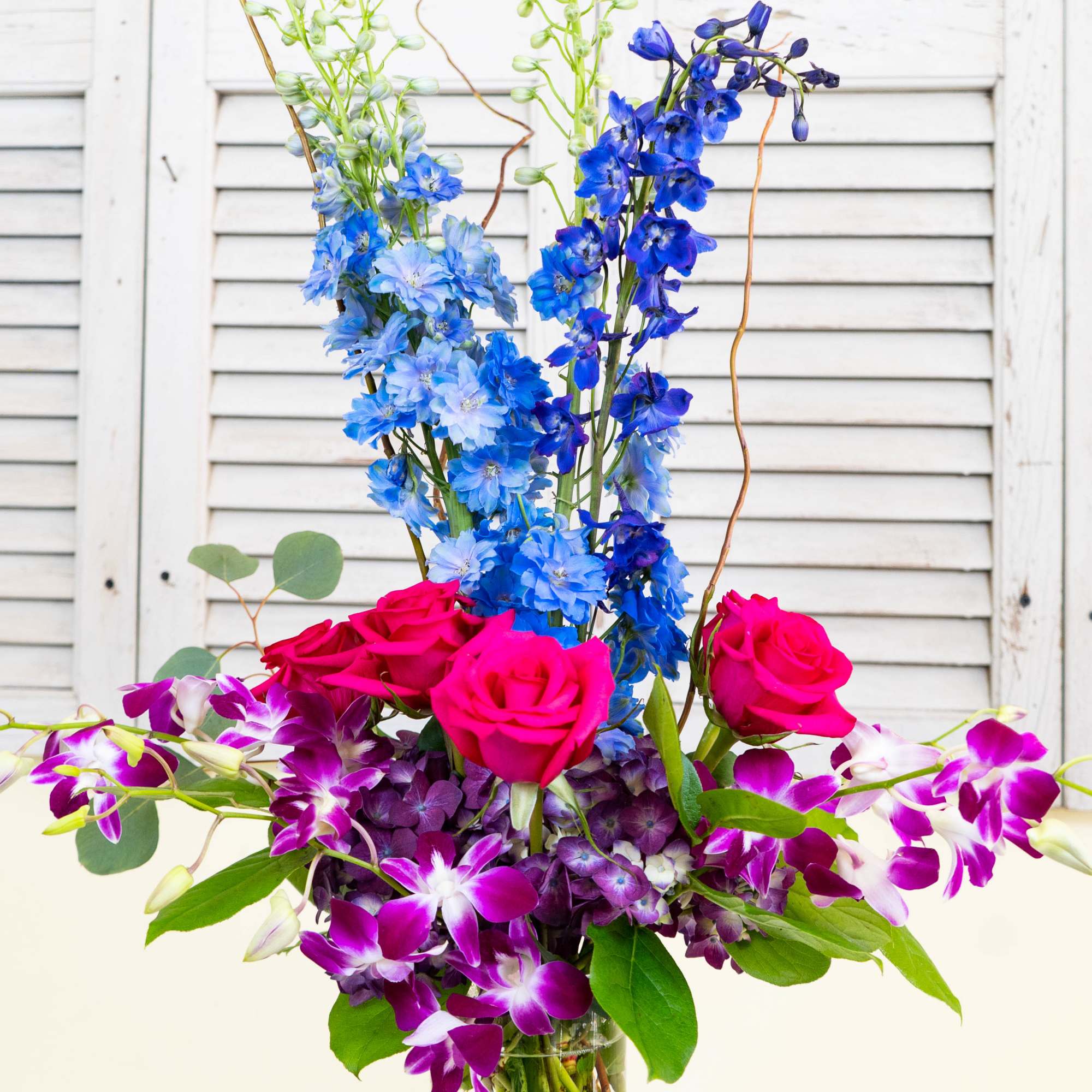 Bouquet of pink roses, blue delphinium, and purple orchids in a glass vase