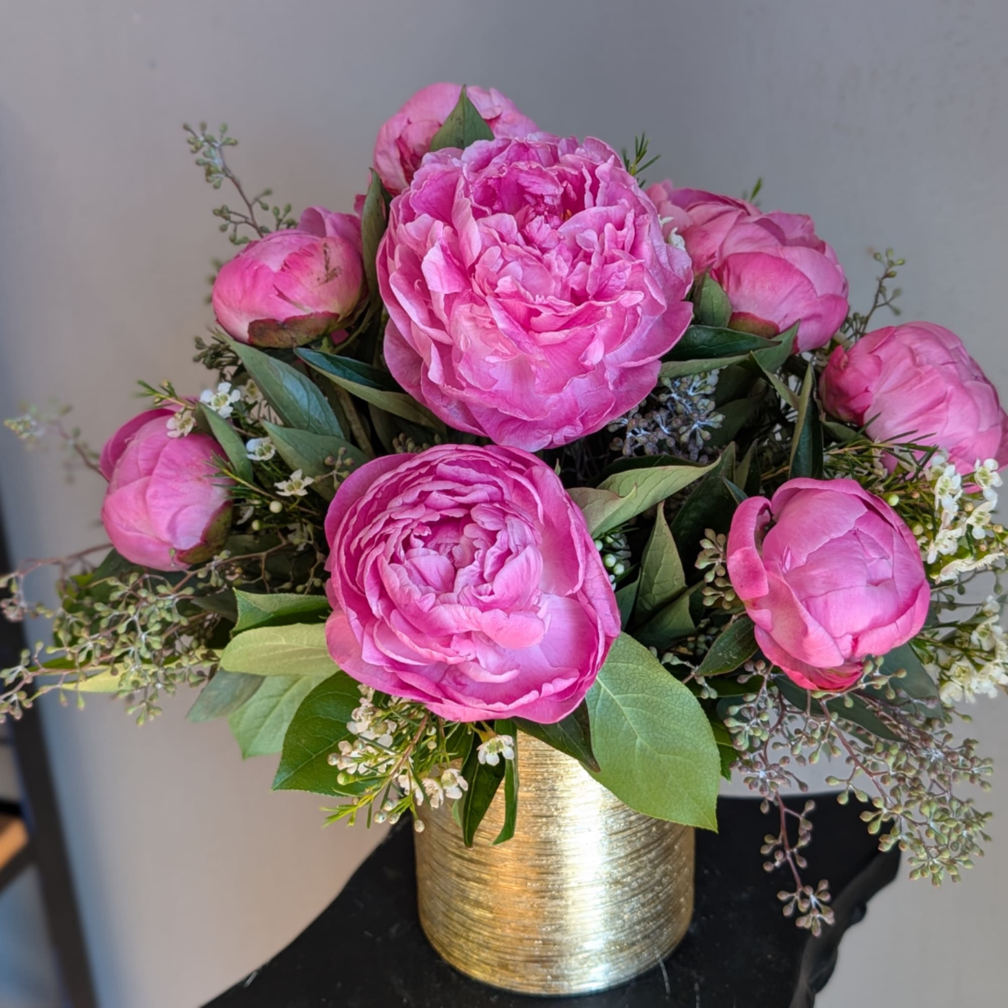 Pink peonies arranged in a gold vase with small white filler flowers