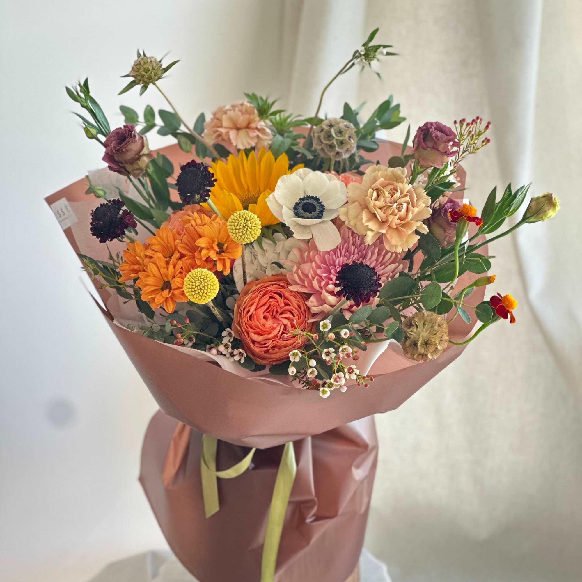 A round bouquet with yellow, orange, green, dark tones, and white flowers