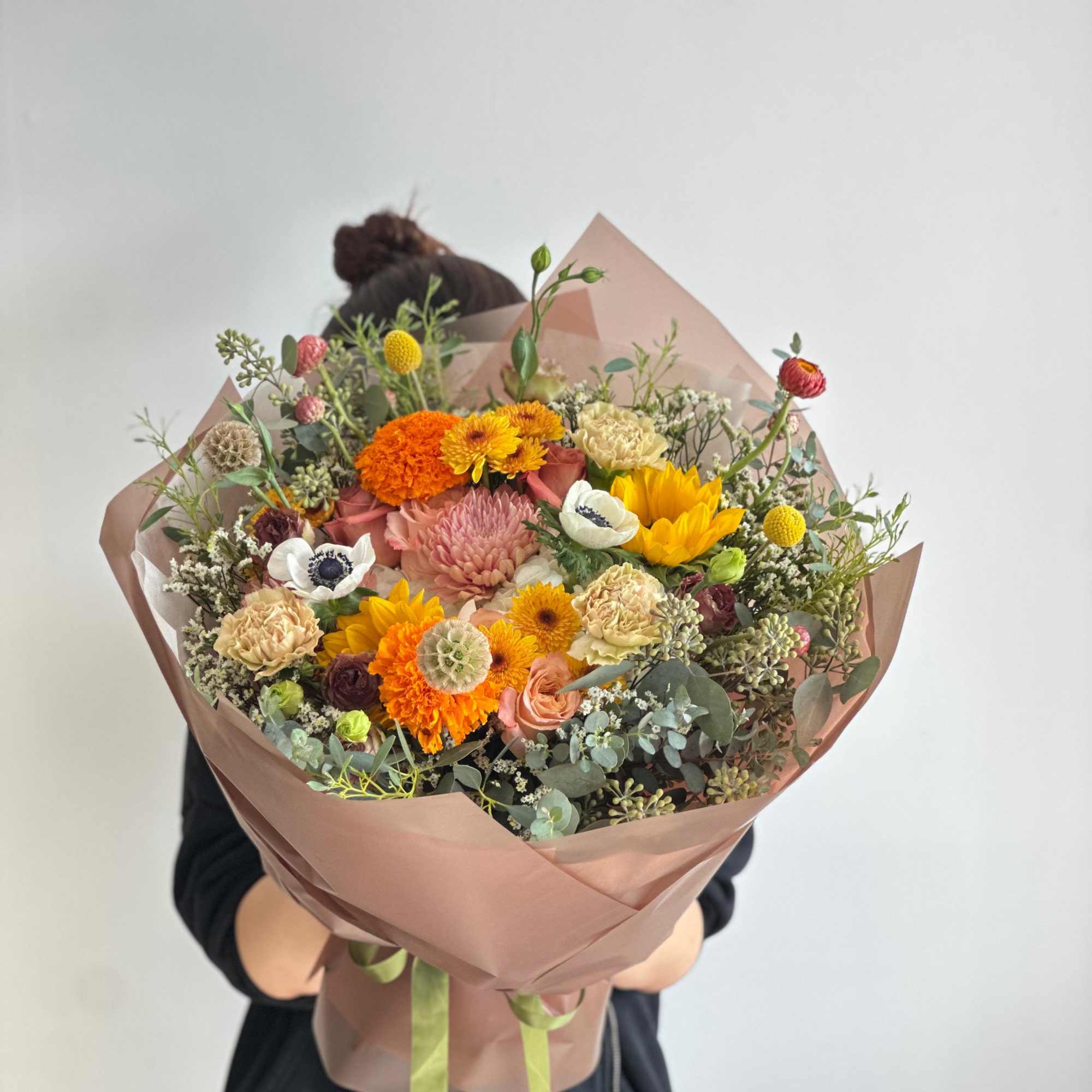 A round bouquet with yellow, orange, green, dark tones, and white flowers