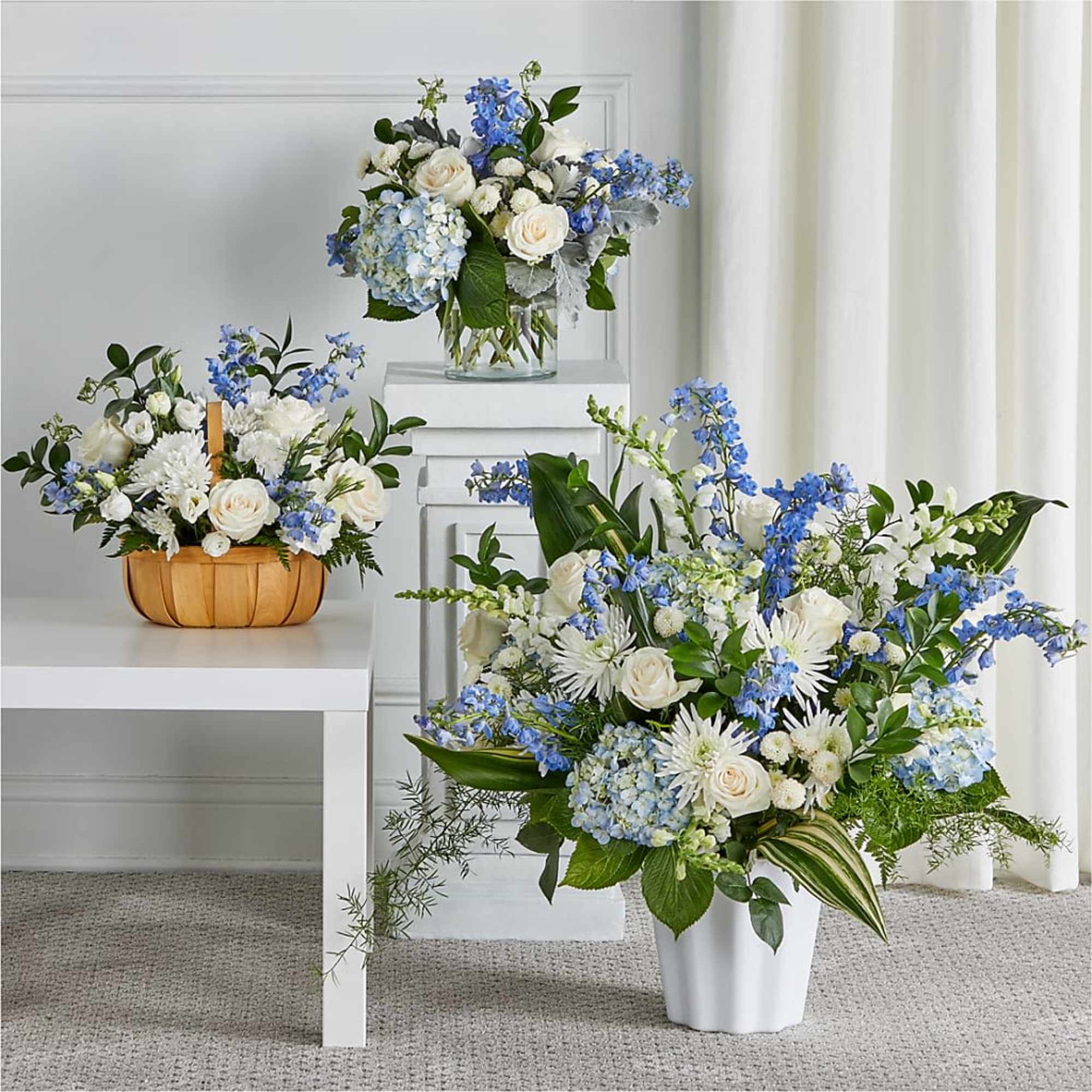 Three blue and white floral arrangements in vases and a basket