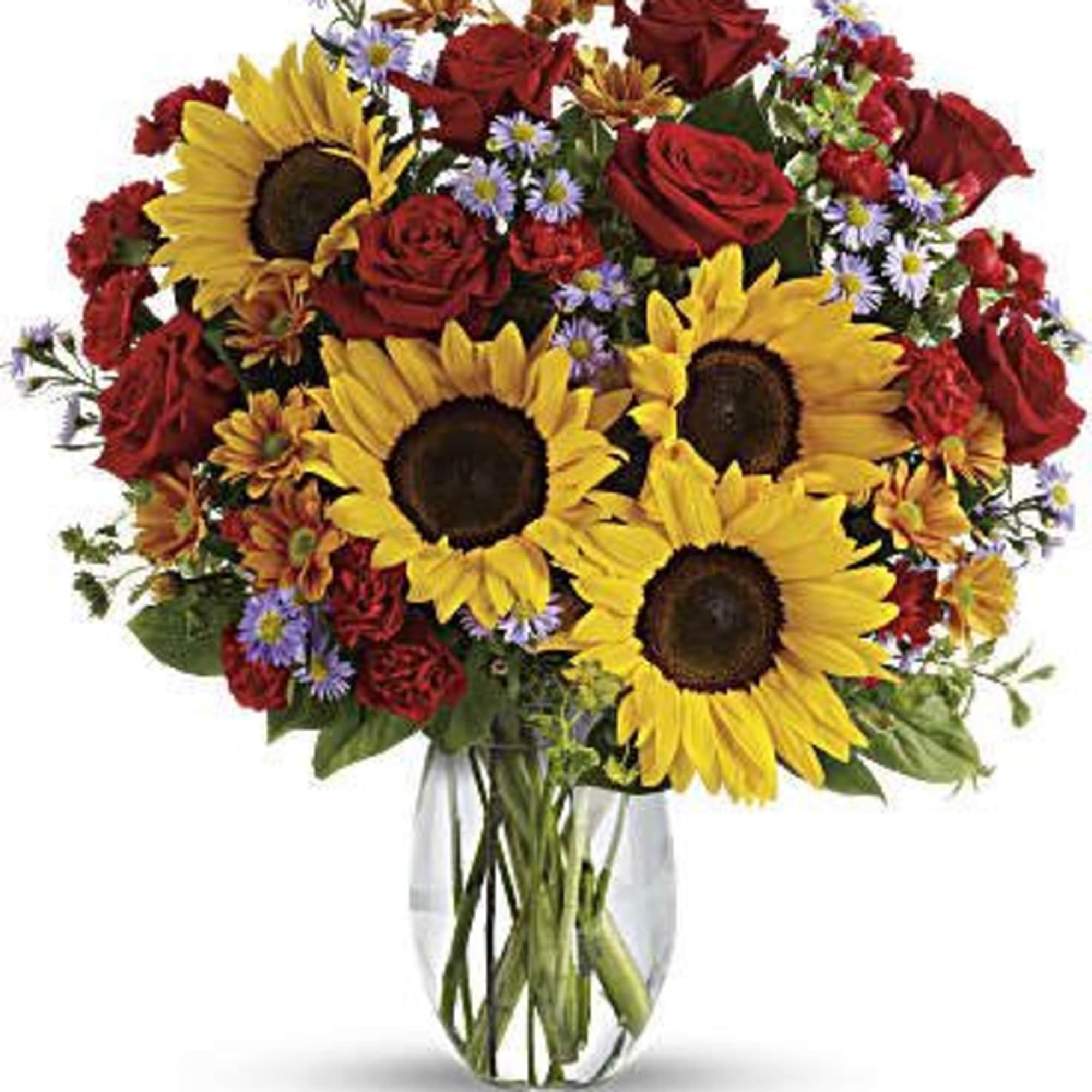 Bouquet of sunflowers, red roses, and small purple flowers in a glass vase