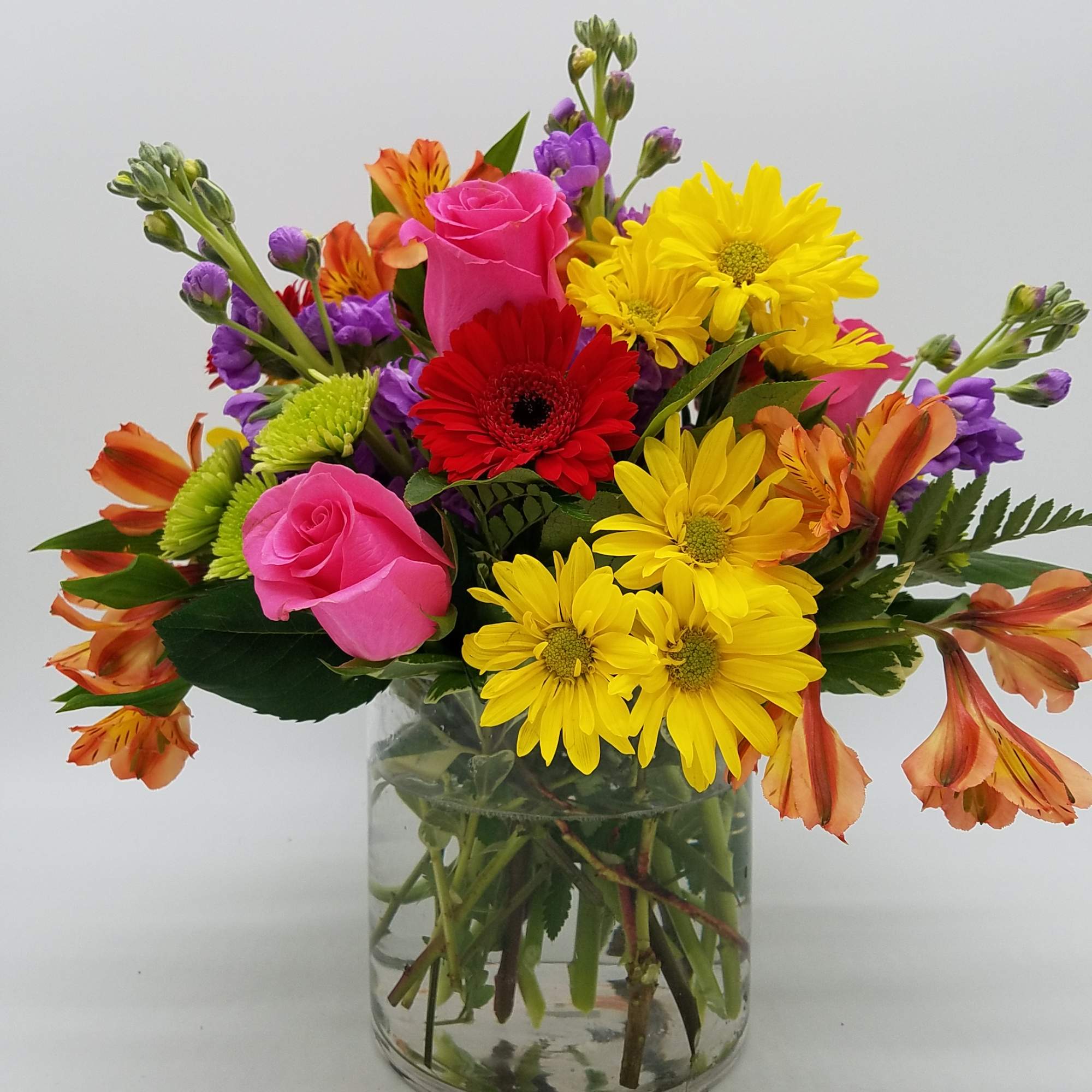 Mixed bouquet of pink roses, yellow daisies, and orange alstroemeria in a glass vase