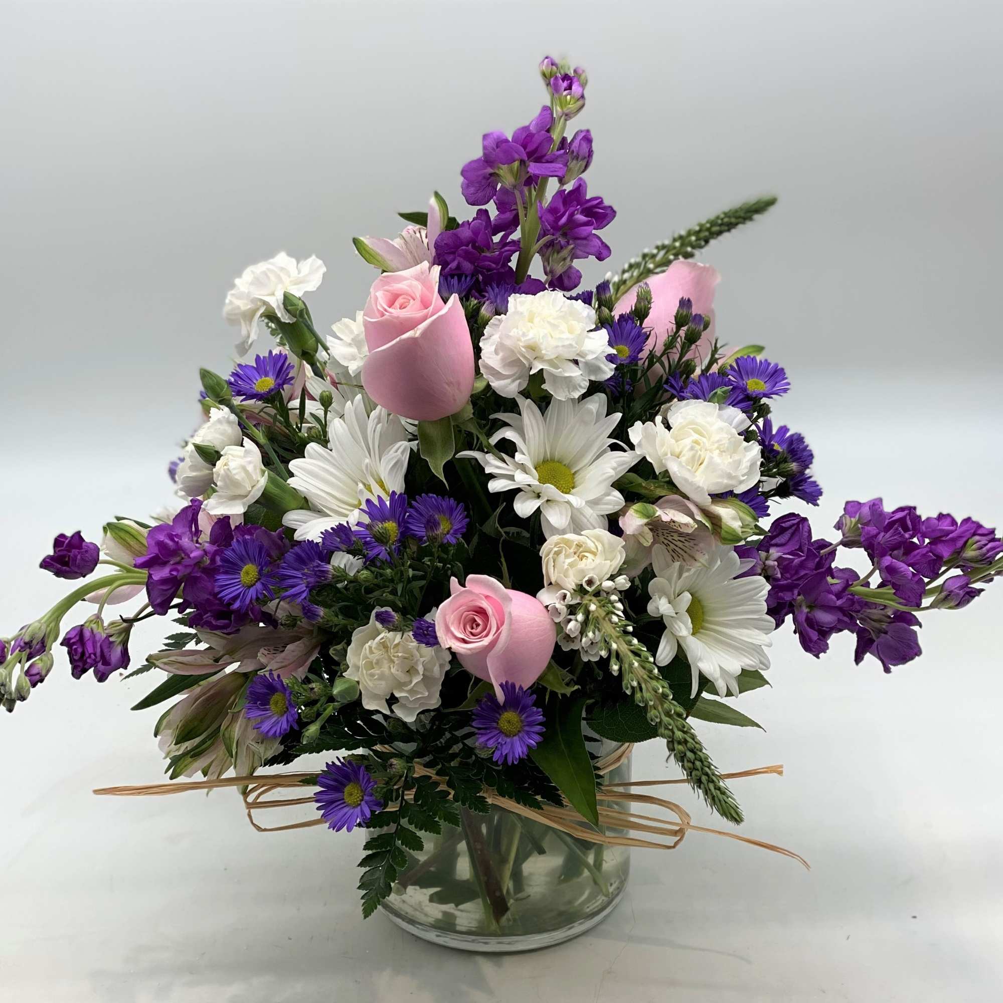 Mixed bouquet of pink roses, white daisies, and purple flowers in a glass vase