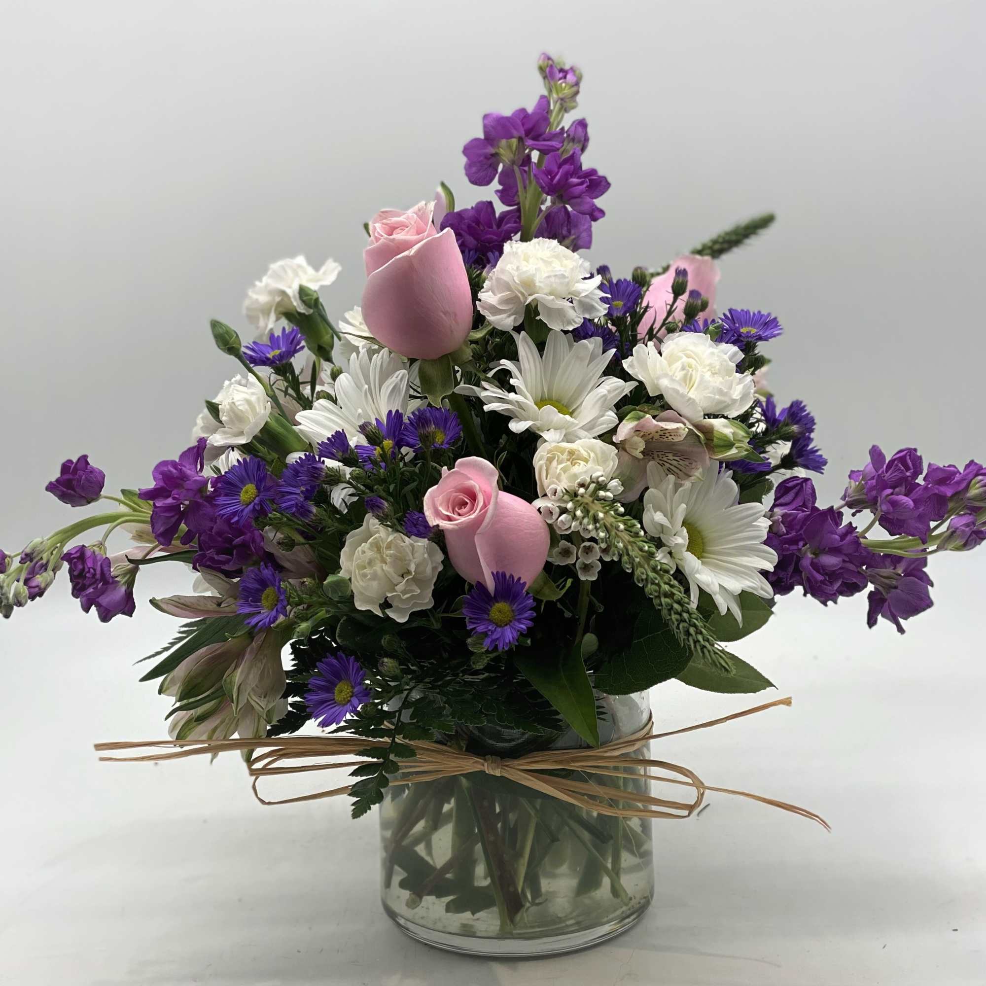 Pink roses and white daisies in a glass vase with purple flowers