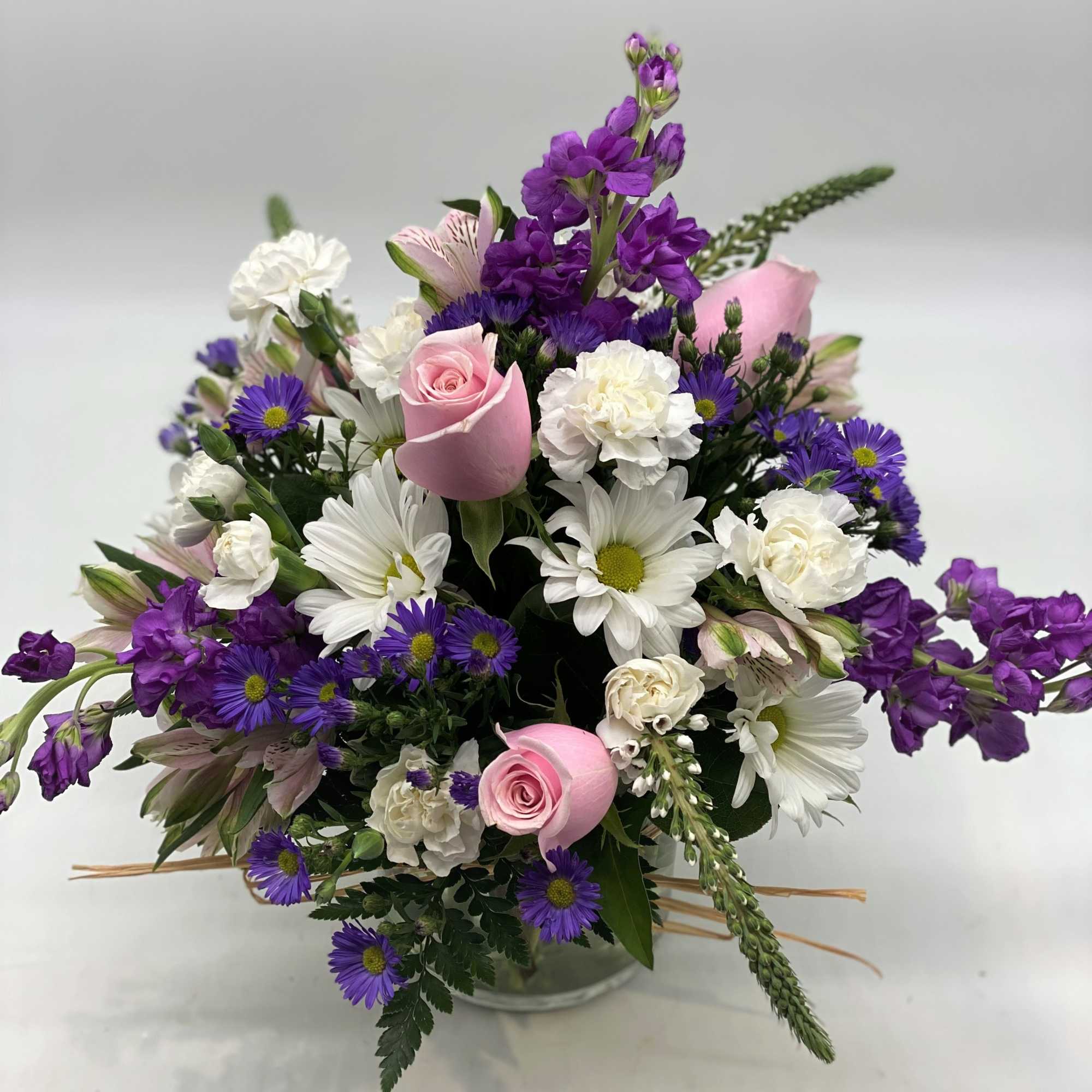 Bouquet of pink roses, white daisies, and purple flowers in a glass vase