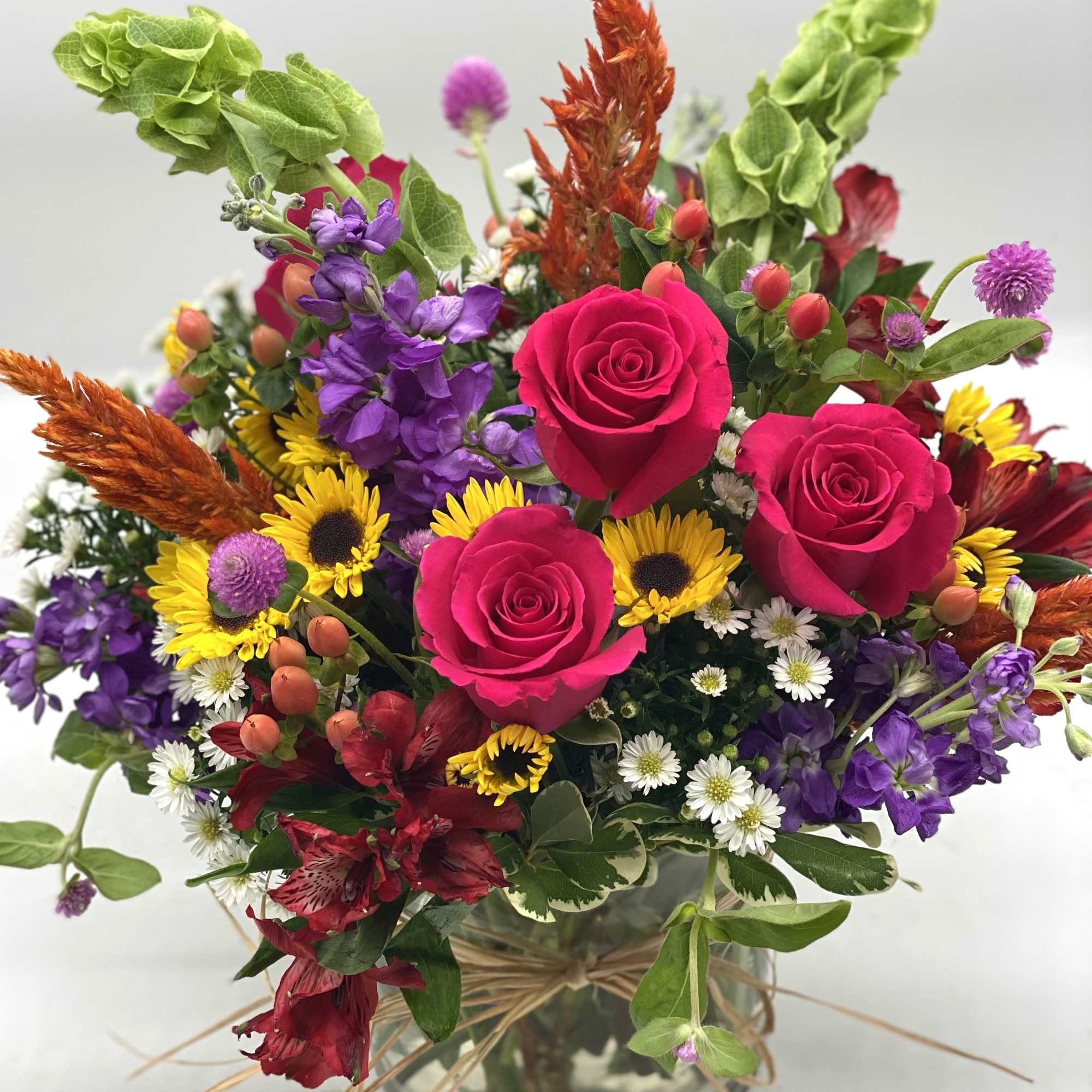 Mixed bouquet of pink roses, sunflowers, and purple flowers in a glass vase