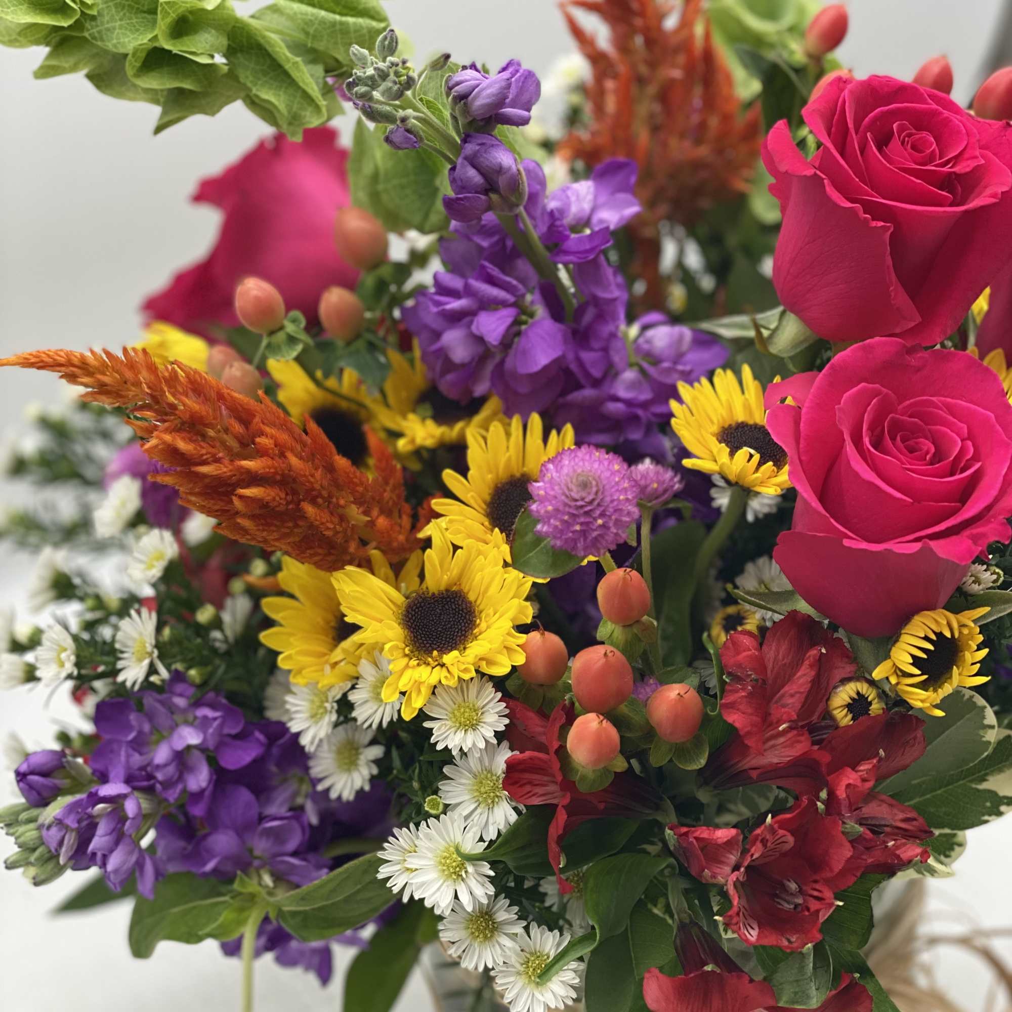 Mixed bouquet with hot pink roses, purple blooms, and yellow sunflowers in a glass vase