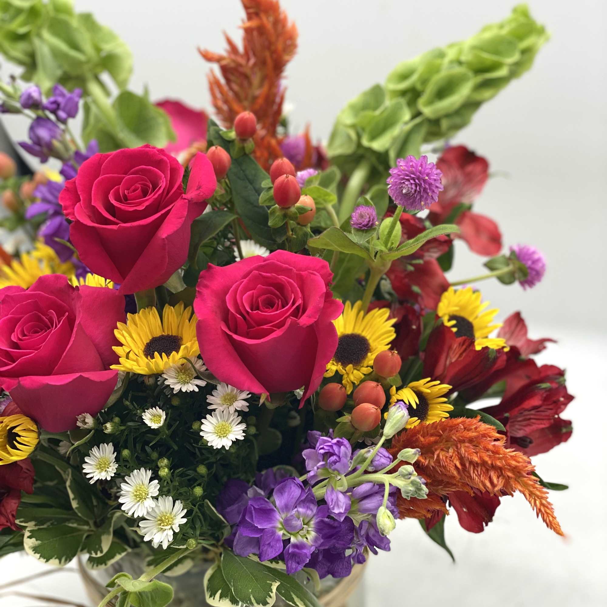 Mixed bouquet with hot pink roses, yellow sunflowers, and purple flowers in a glass vase