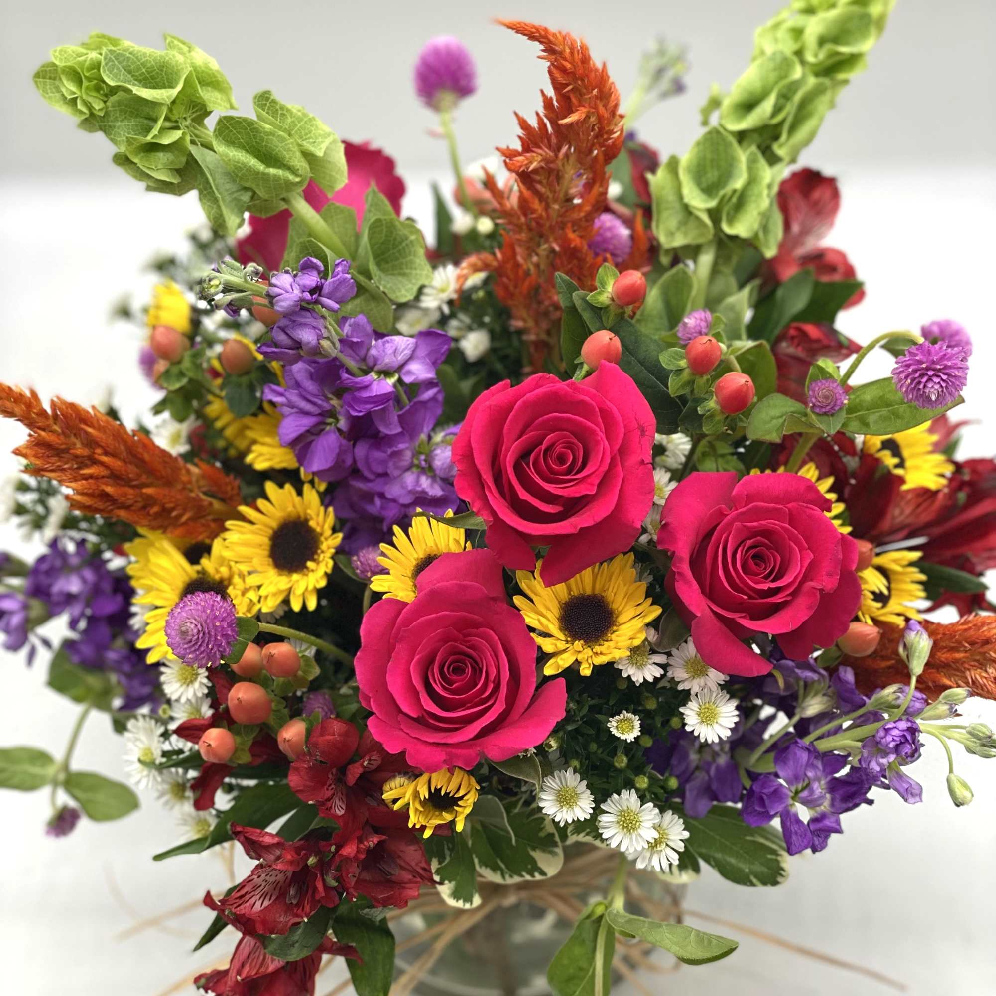 Mixed bouquet with hot pink roses, yellow daisies, and purple flowers in a glass vase