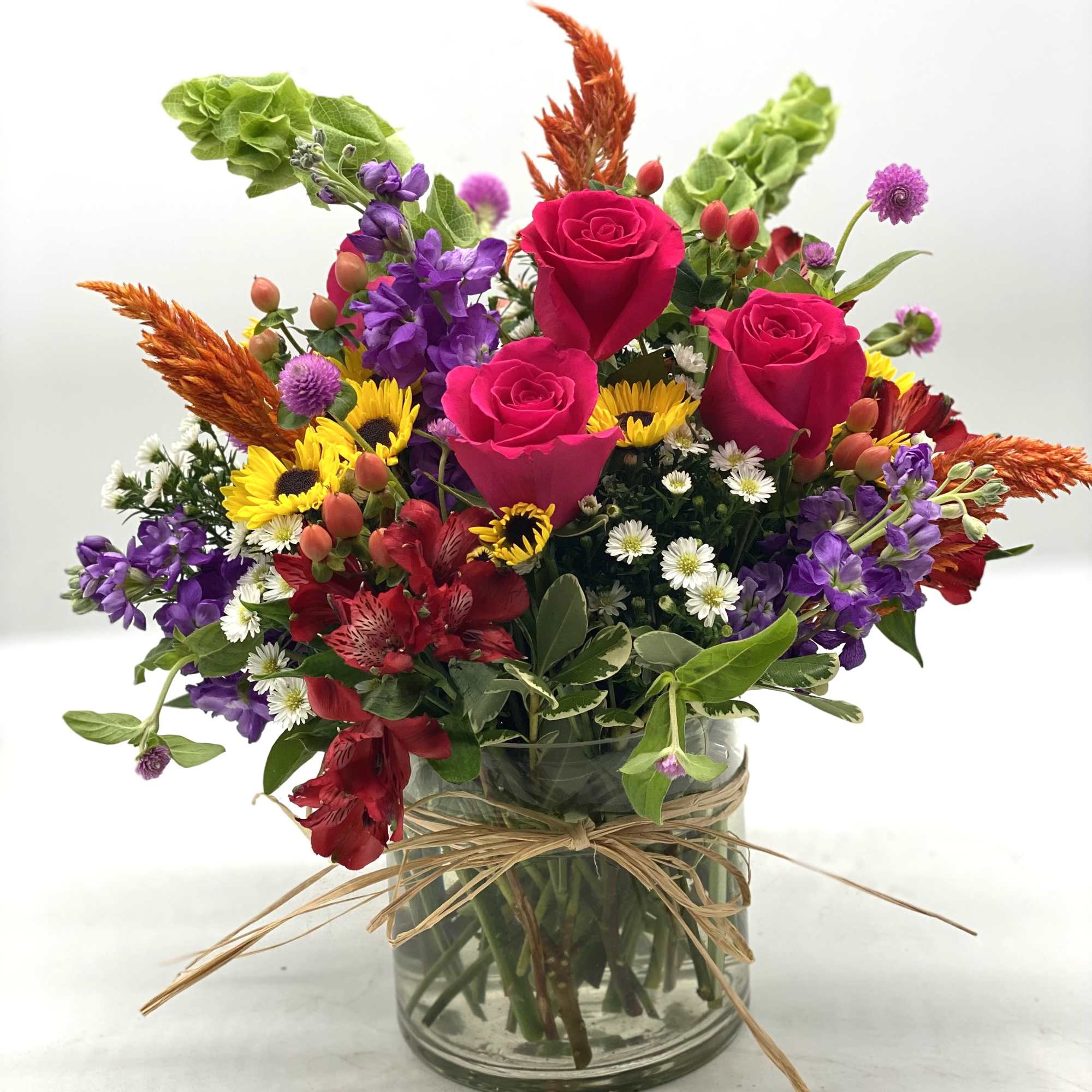 Mixed bouquet of roses, sunflowers, and purple flowers in a glass vase