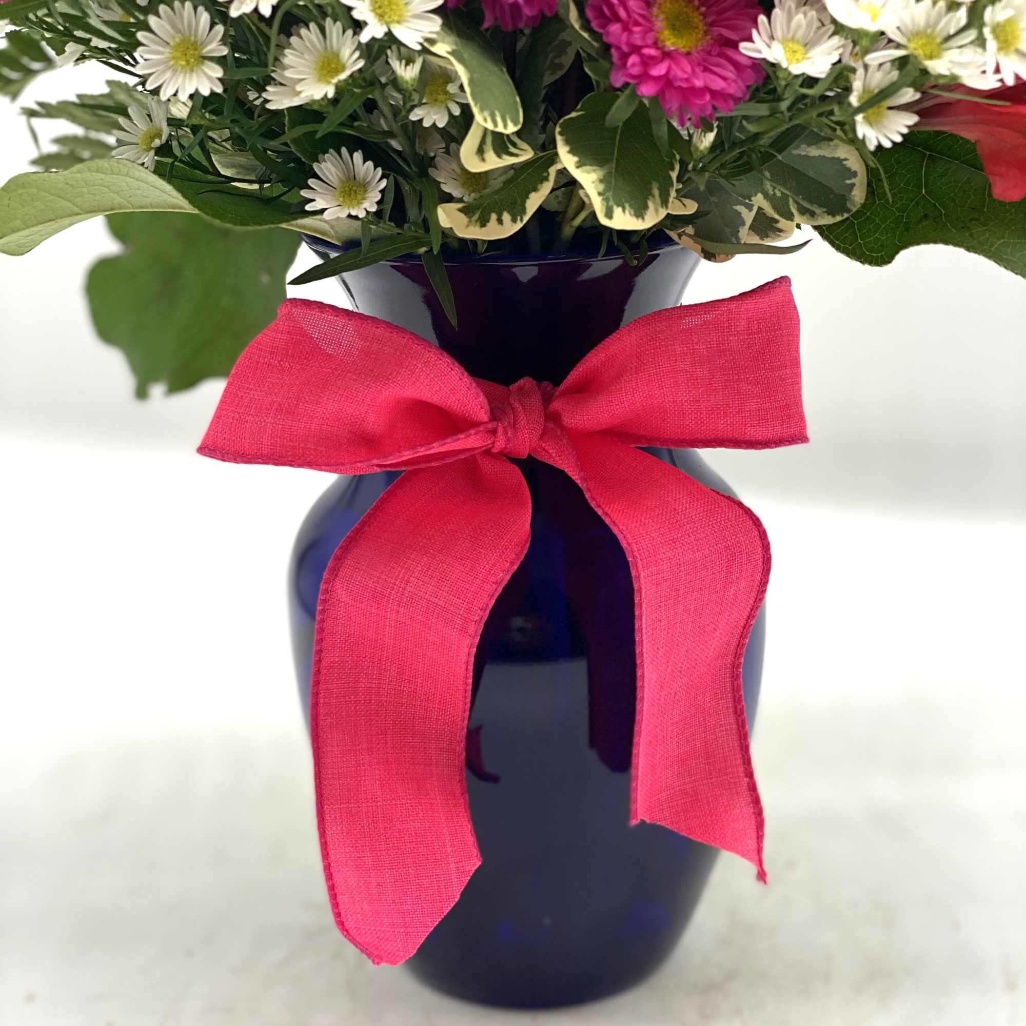 Mixed white and pink flowers in a dark blue vase with a pink bow