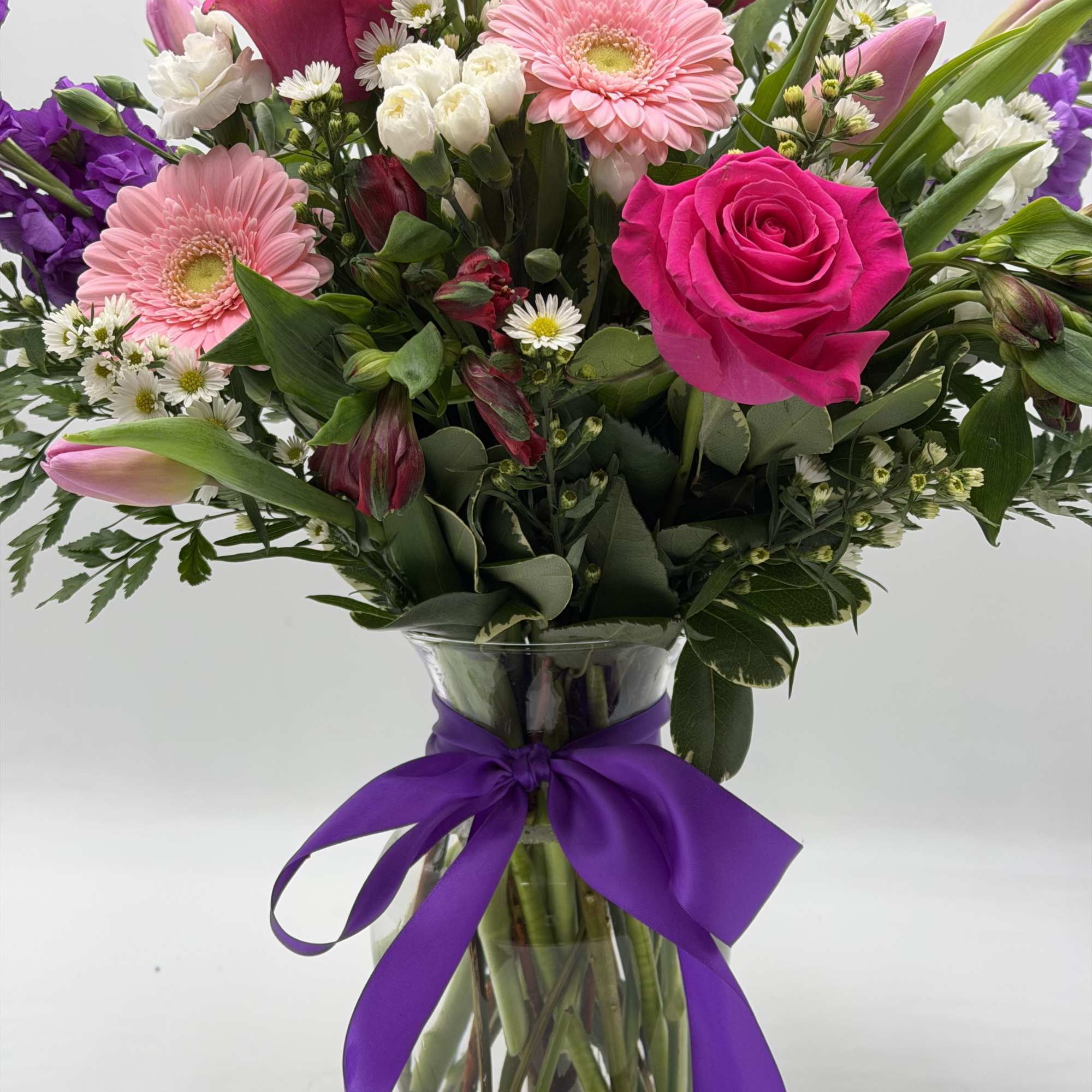 Pink roses and gerbera daisies in a glass vase with a purple ribbon