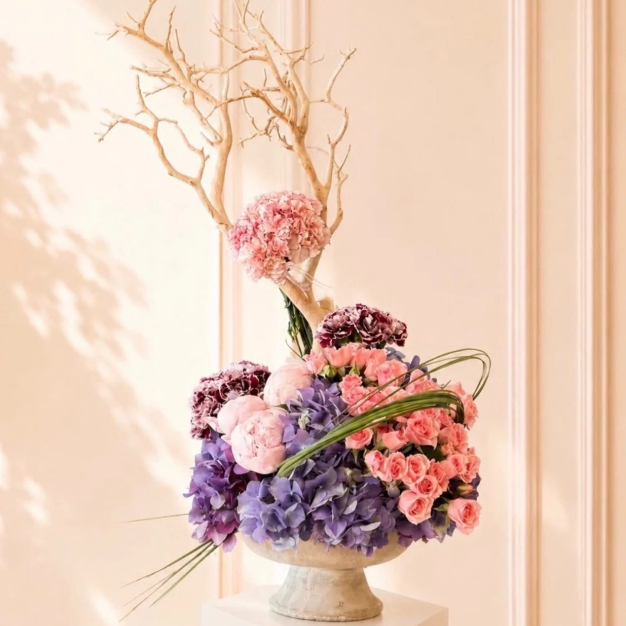 Pink and purple floral arrangement in a pedestal vase with bare branches