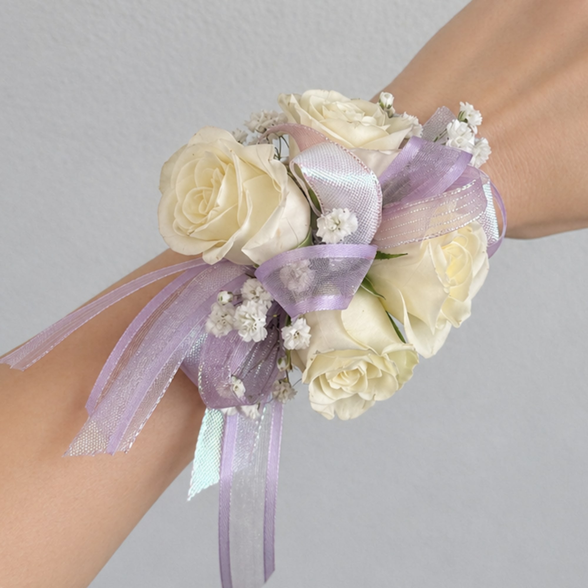 Cream rose wrist corsage with lavender ribbon on a person's wrist