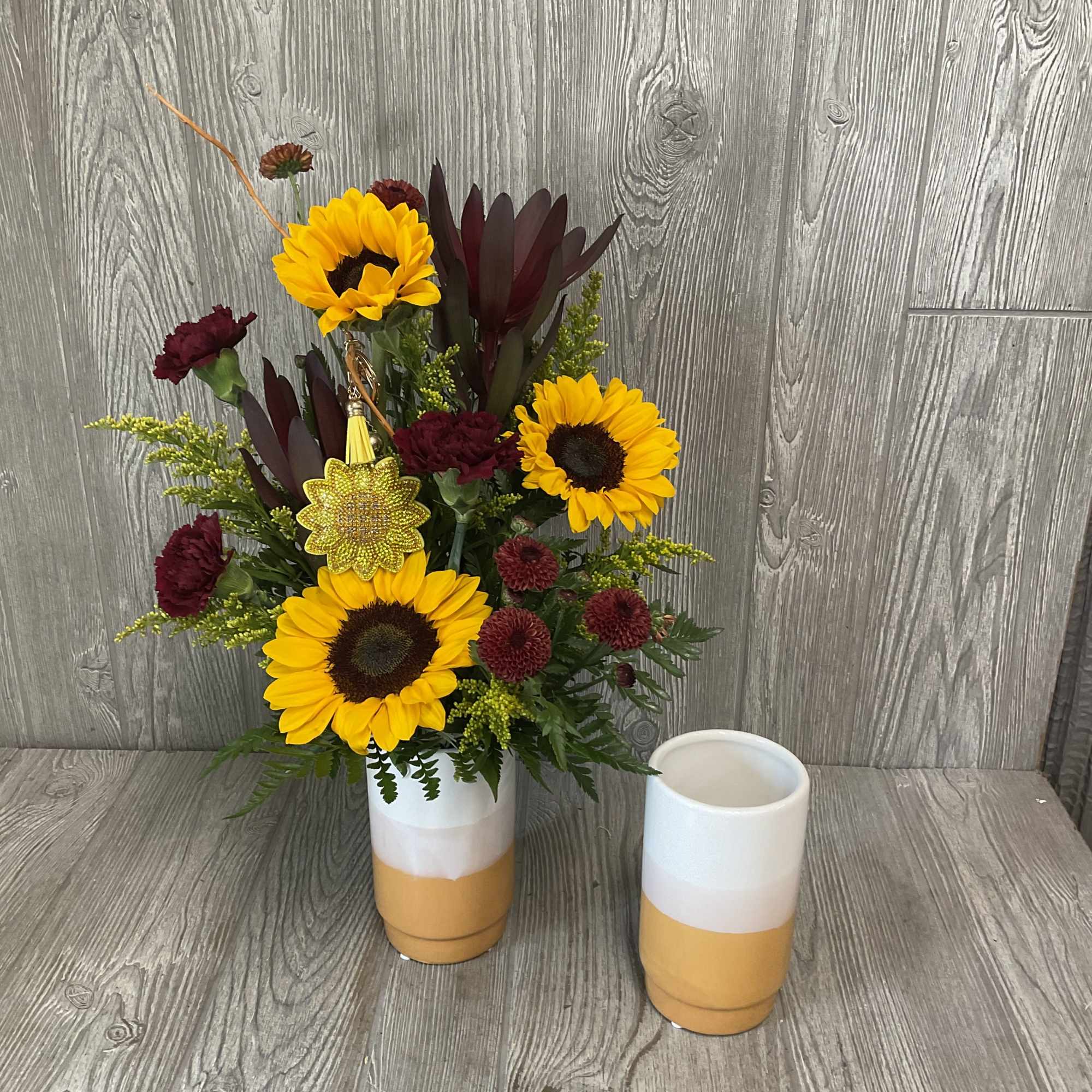 Sunflowers and burgundy flowers arranged in a two-tone vase.