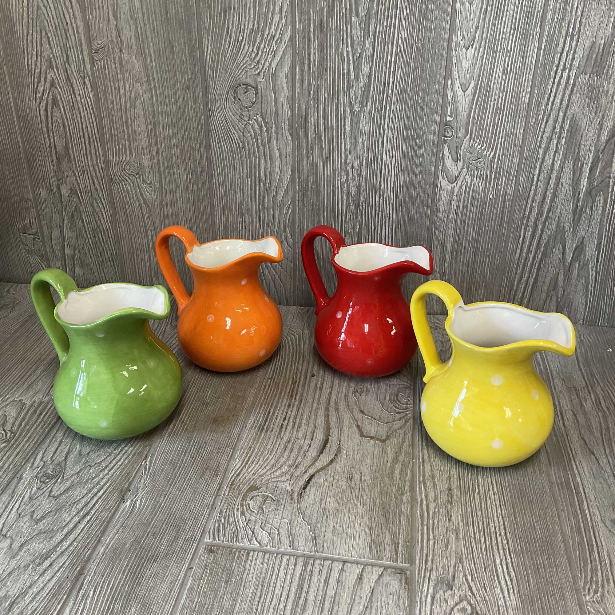 Four colorful ceramic pitchers with white interiors on a wood floor