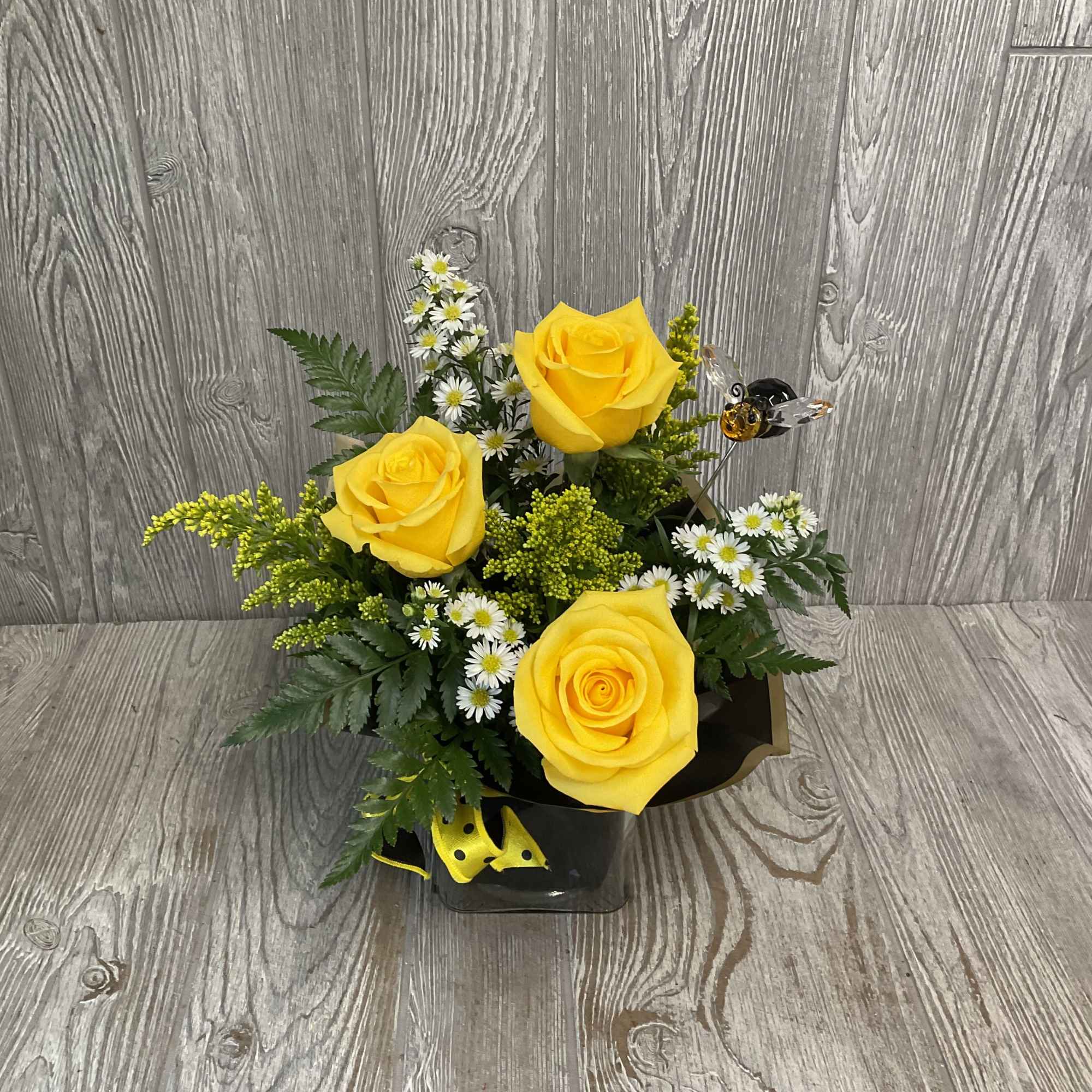 Yellow roses arranged with small white daisies in a black container.