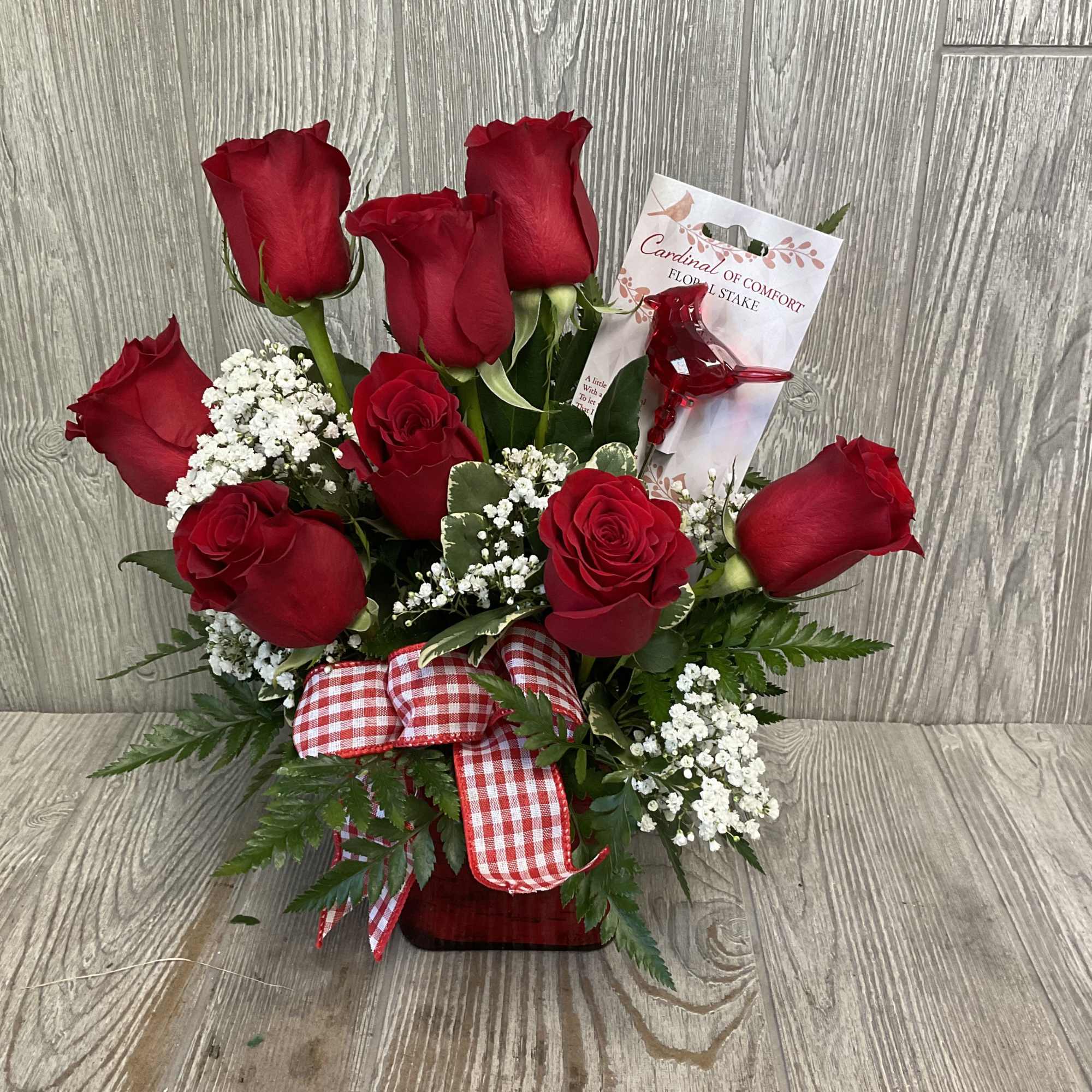 Red rose arrangement with baby's breath in a red vase with gingham bow and cardinal pick.