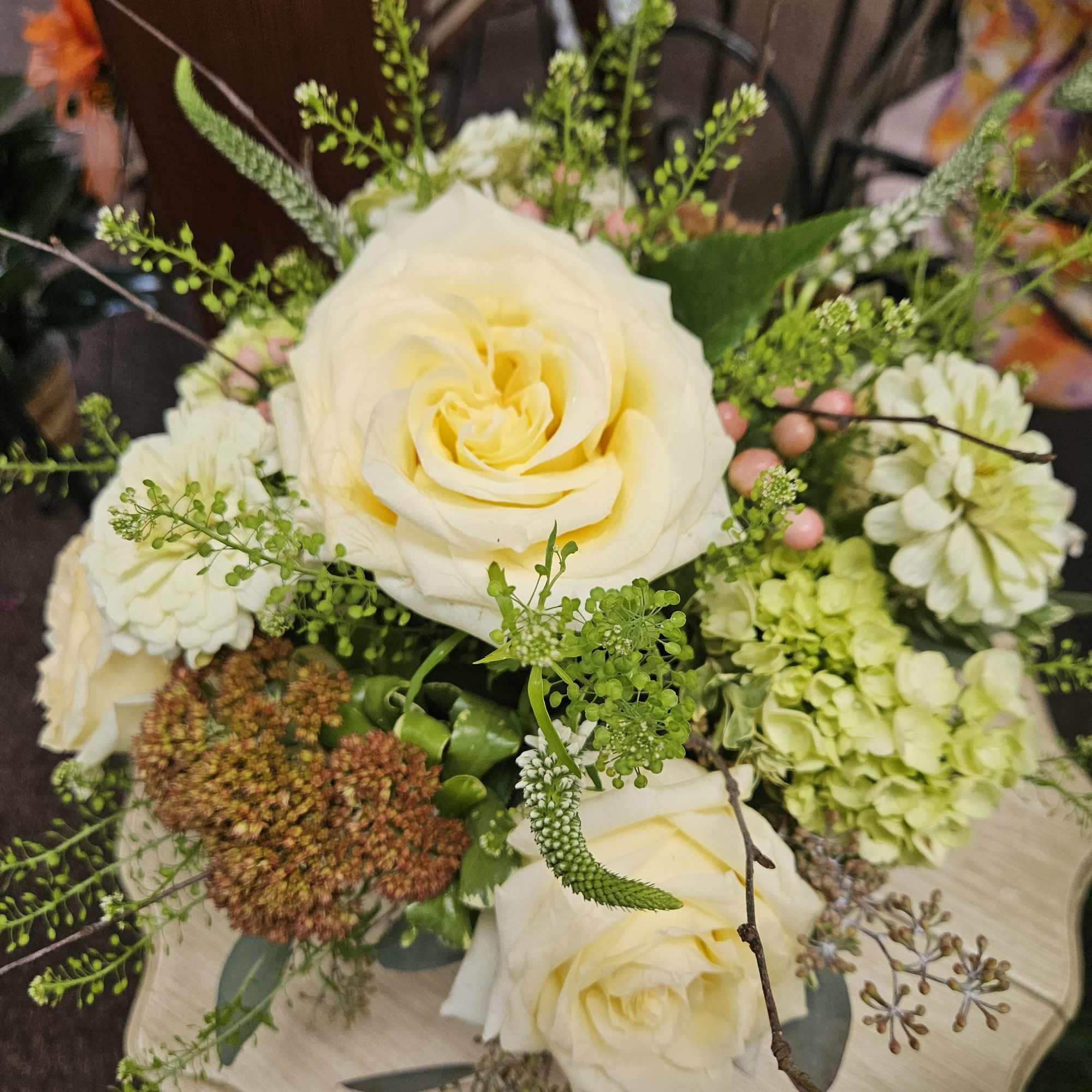 Compact arrangement of pale yellow roses with green hydrangea and accent blooms on a light pedestal stand
