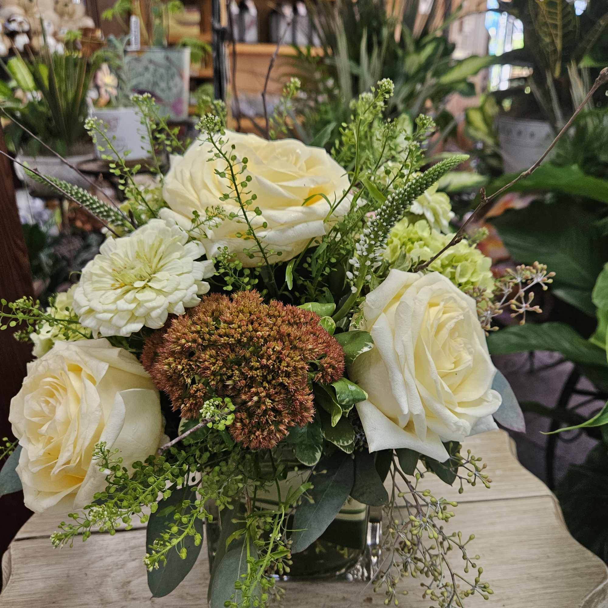 Low arrangement of ivory roses and mixed blooms in a clear glass cube vase on a light wood table