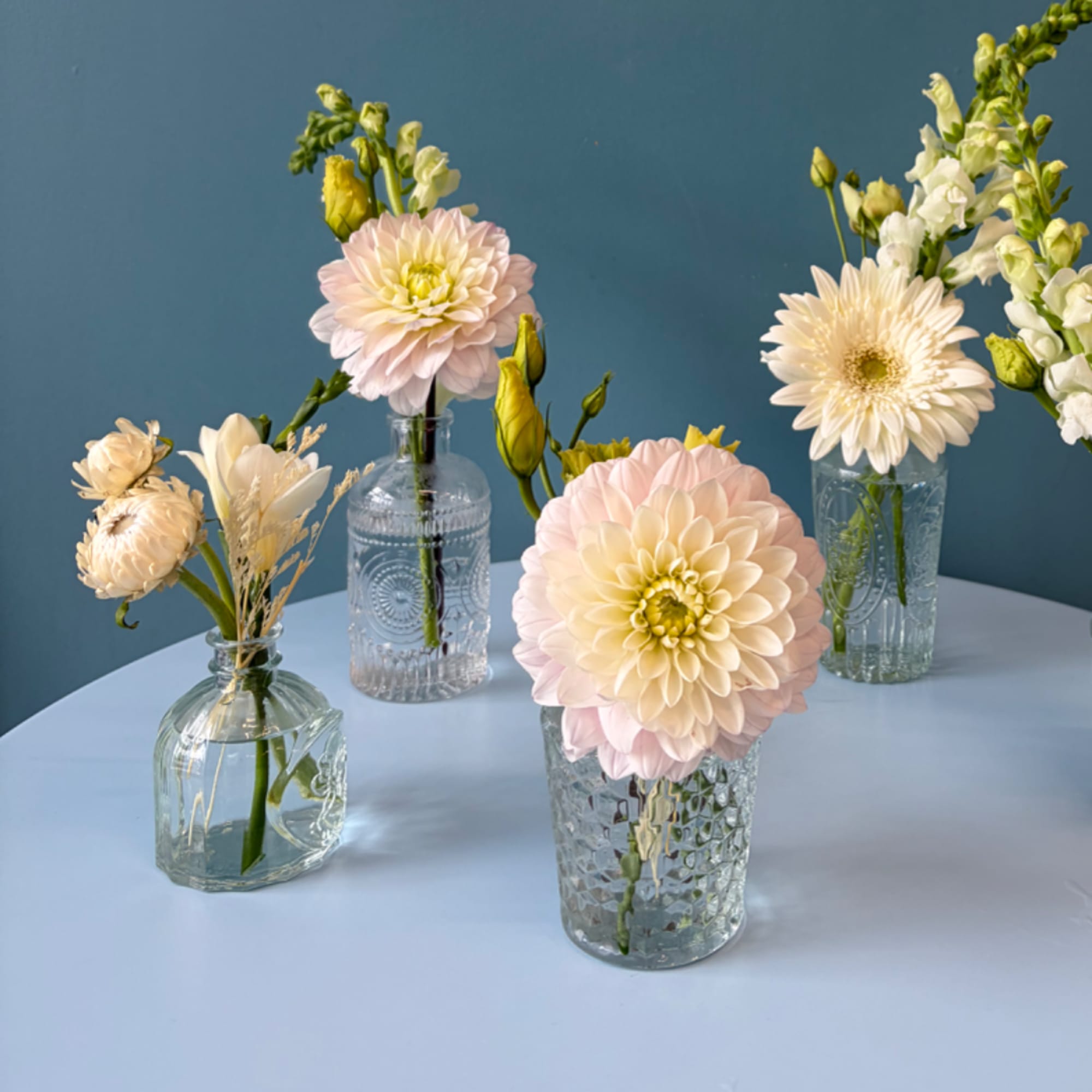 Pastel flowers arranged in small glass vases on a blue table