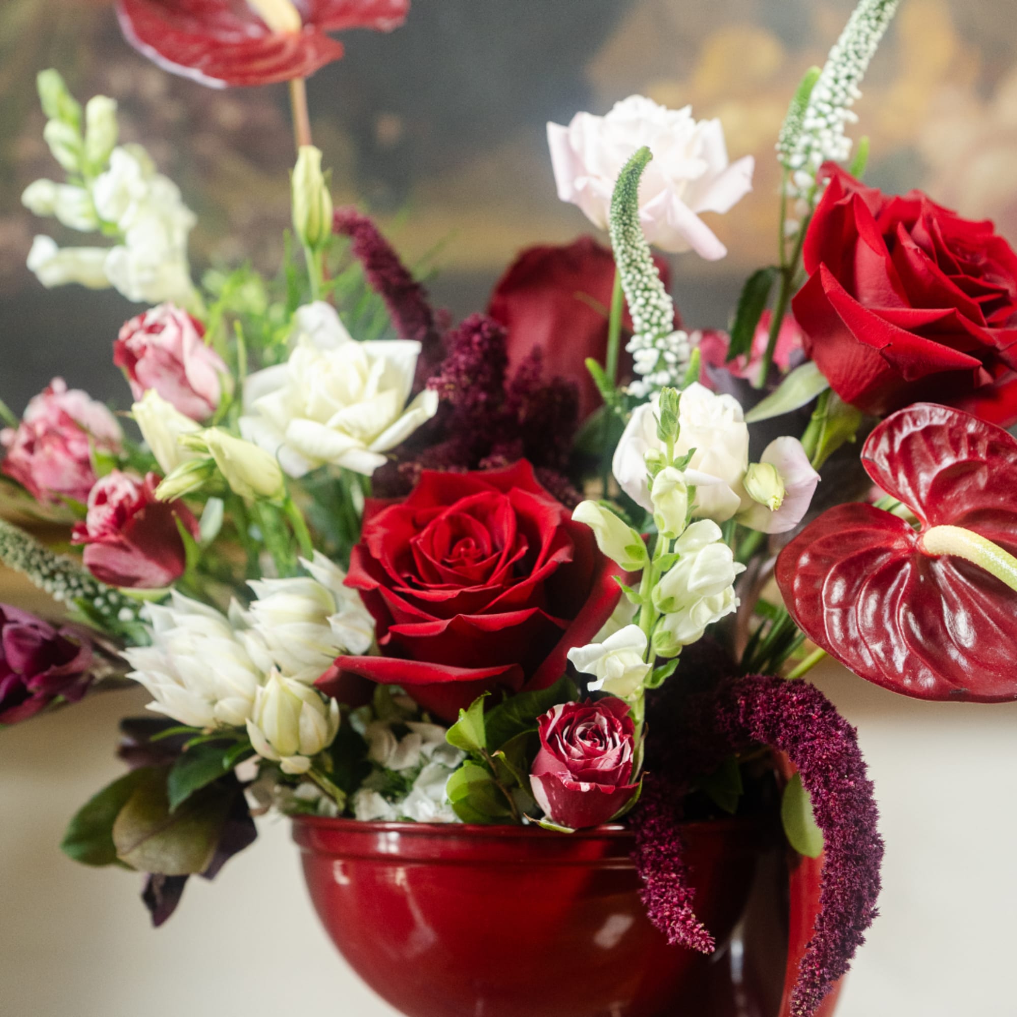 Red and white floral arrangement in a red bowl vase