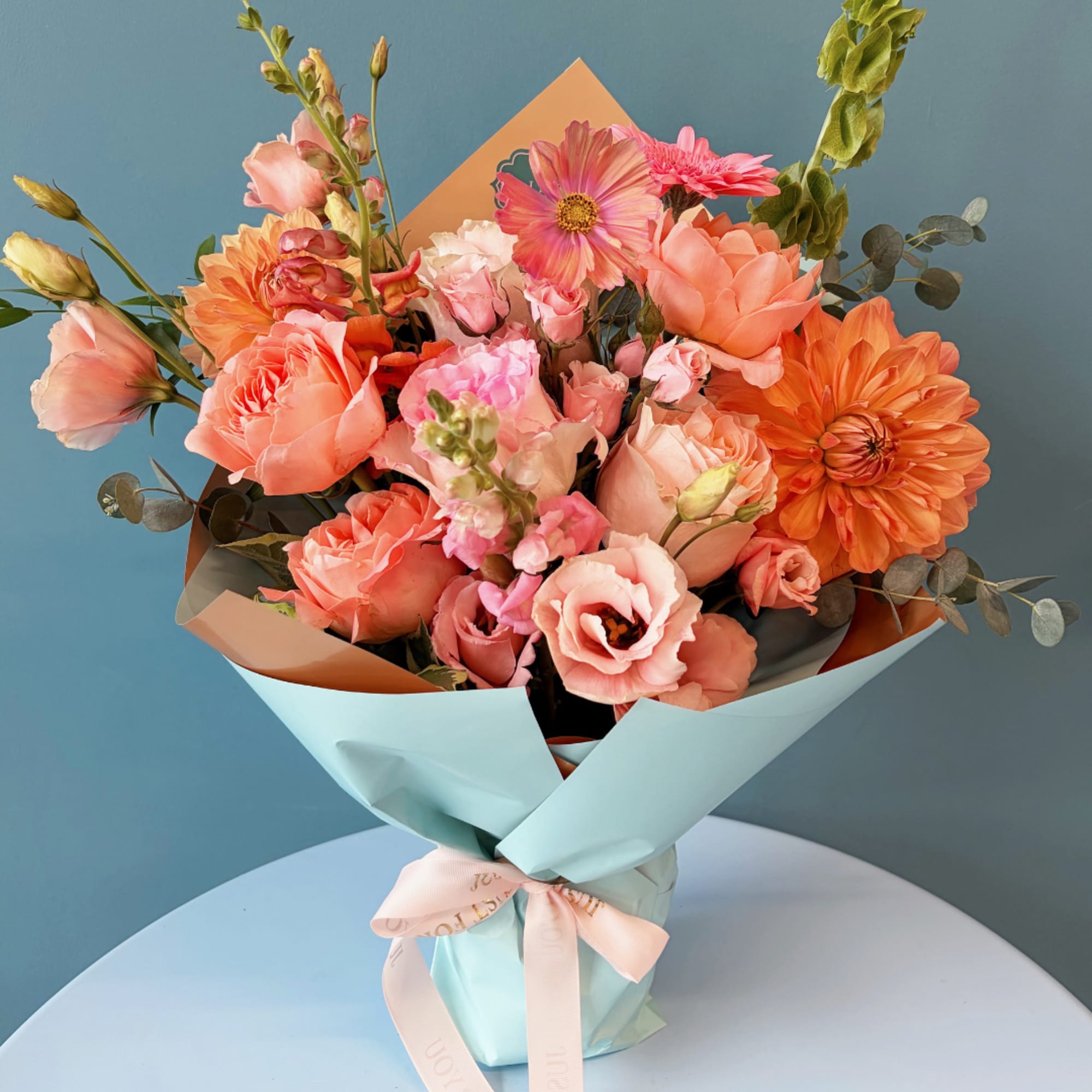 Bouquet of peach and pink flowers wrapped in light blue paper