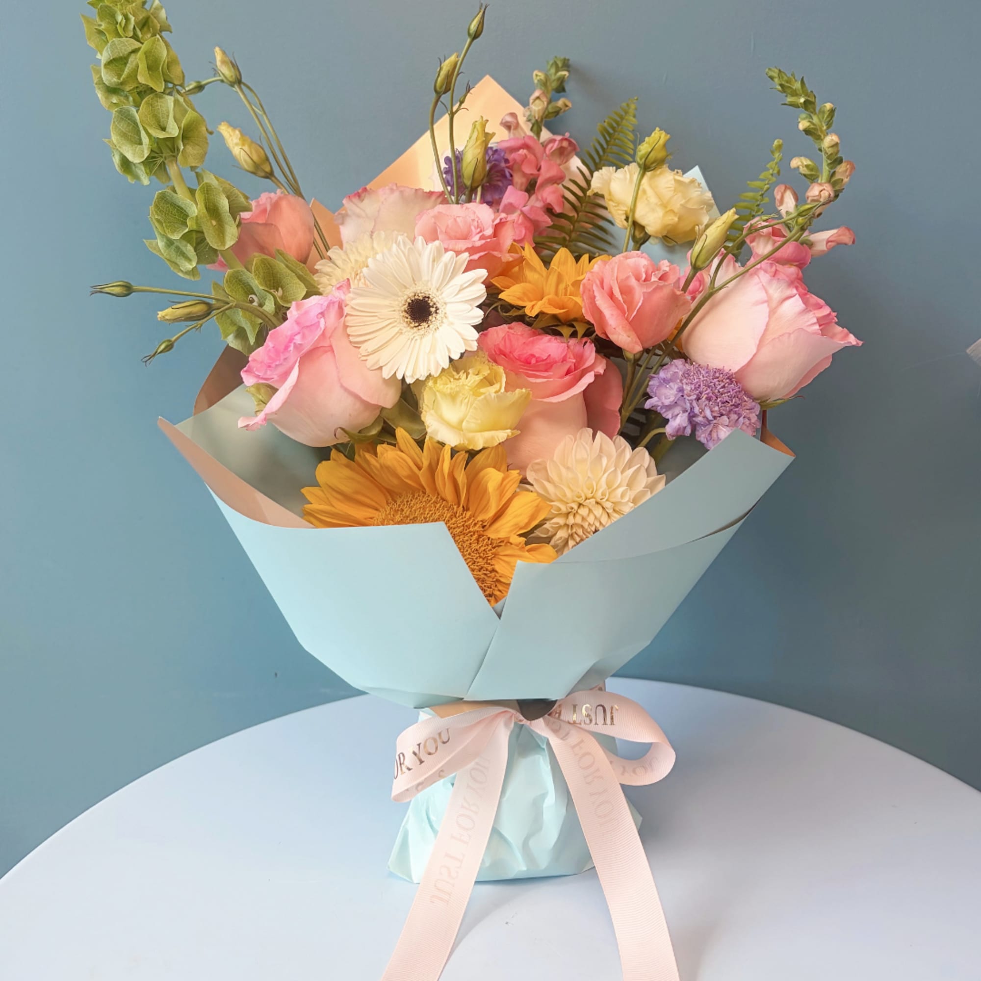 Mixed bouquet of pastel roses, gerbera daisies, and other blooms wrapped in blue paper