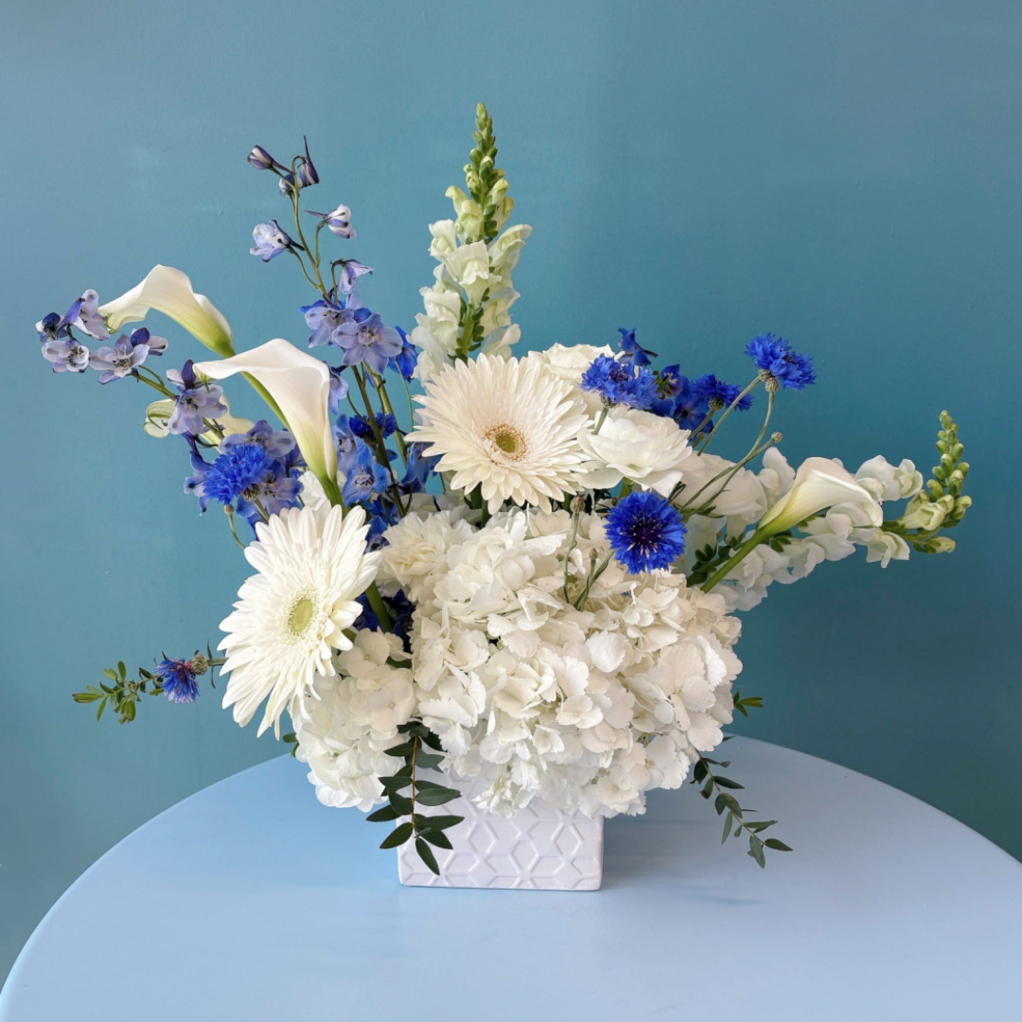 White and blue floral arrangement in a white square vase